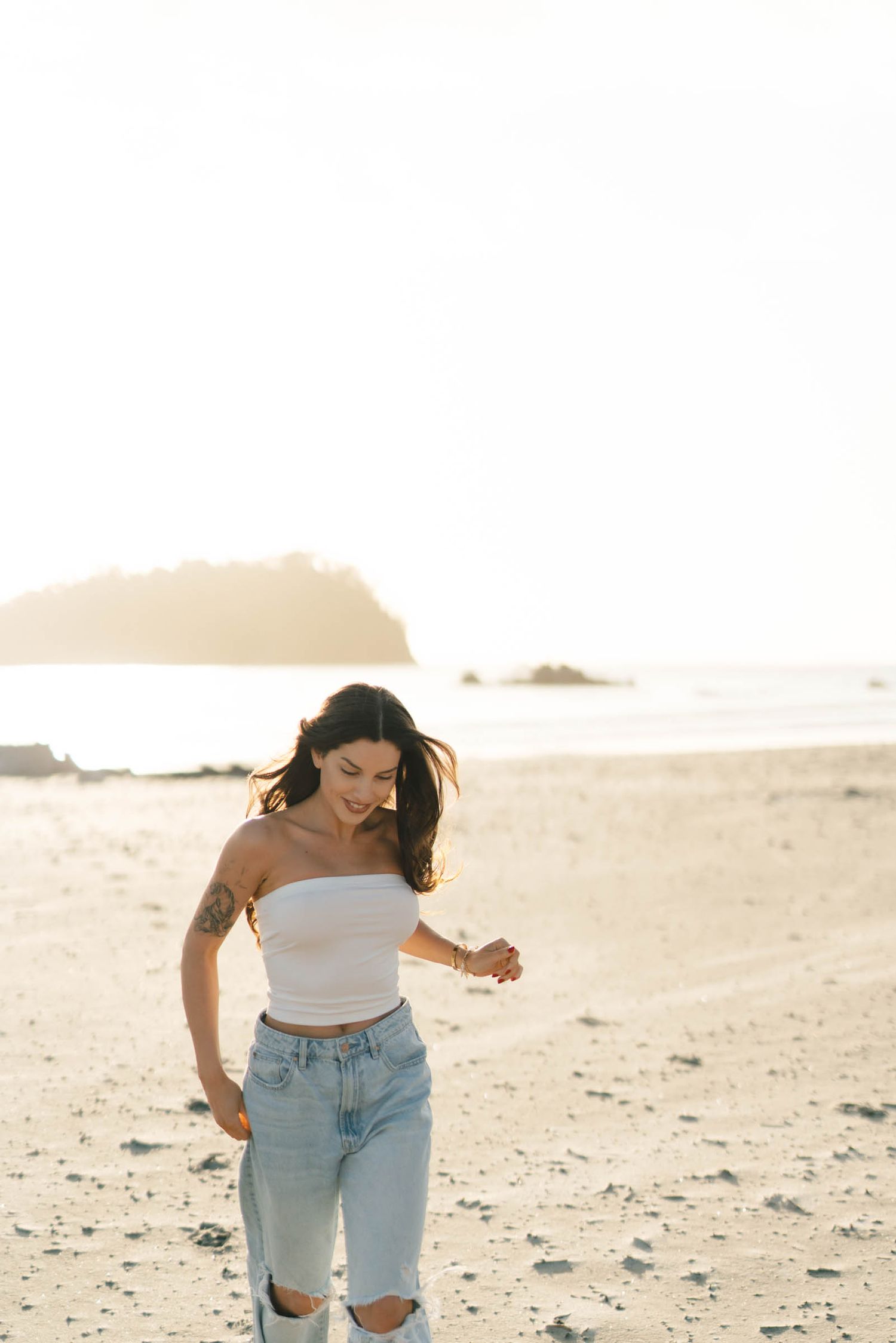 A person in ripped jeans and crop top dances on a beach during sunset.