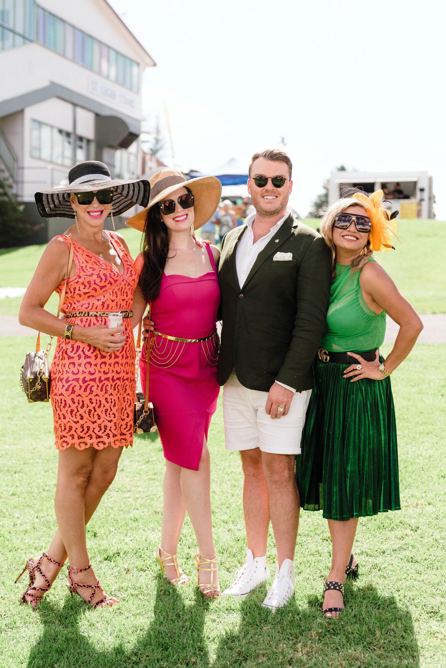 Friends in vibrant dresses and sunglasses gather for photos at an outdoor summer event.