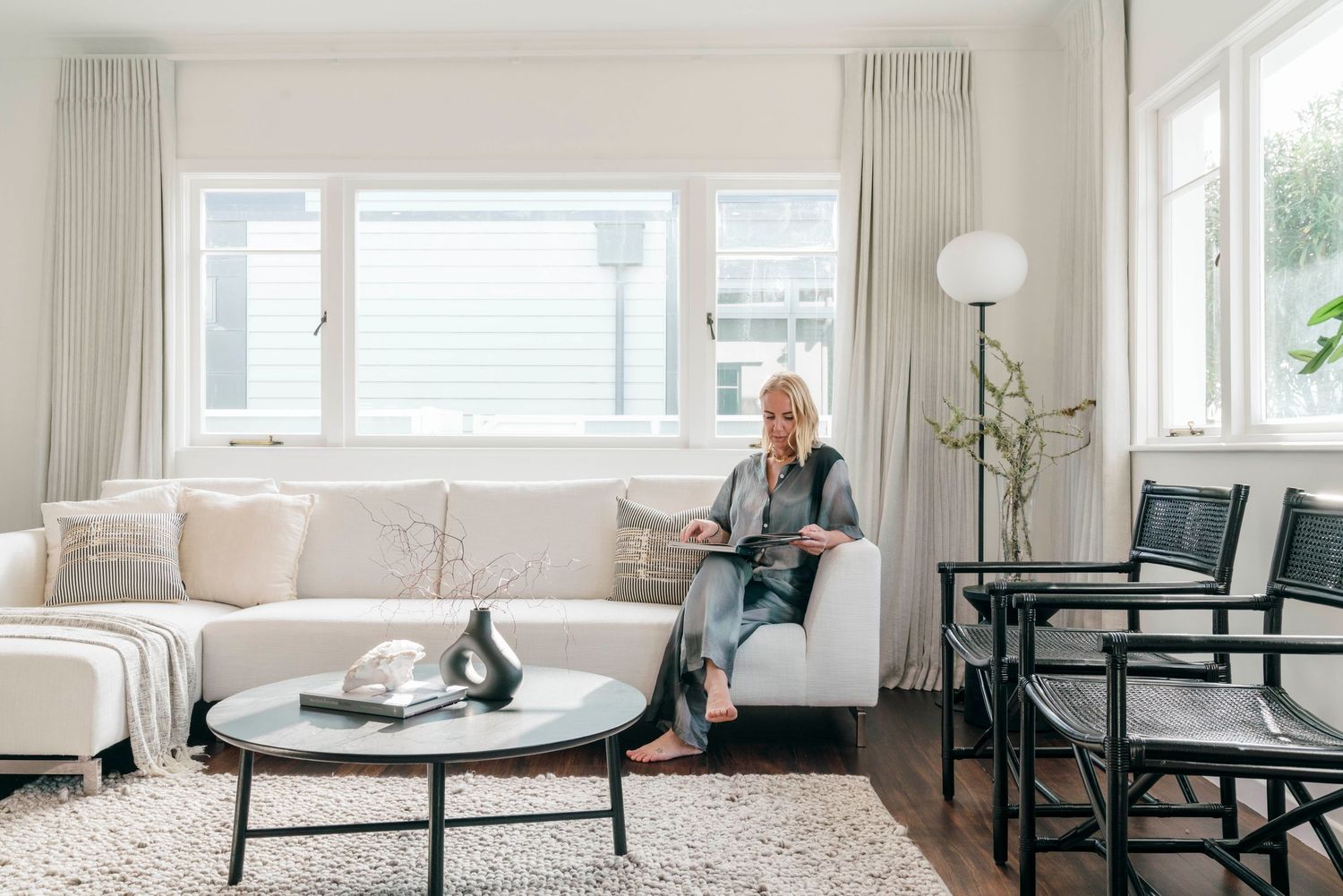 Bright modern living room with a white sectional sofa, round coffee table and globe floor lamp by large windows.