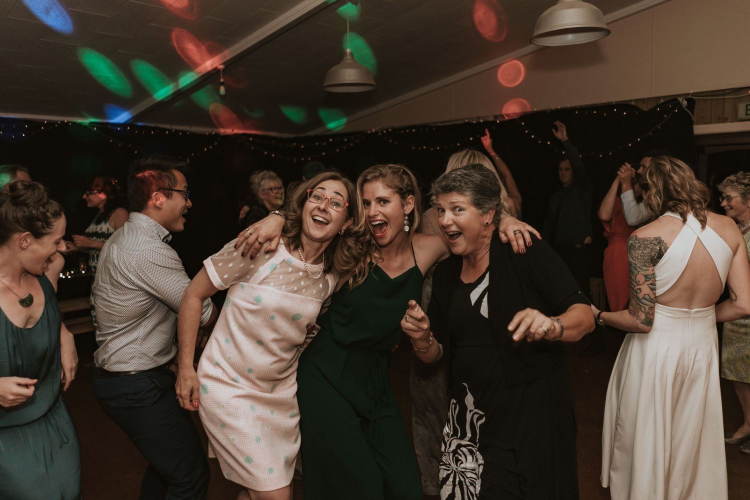 People dancing joyfully at a wedding reception with colorful lights and decorative ambiance.