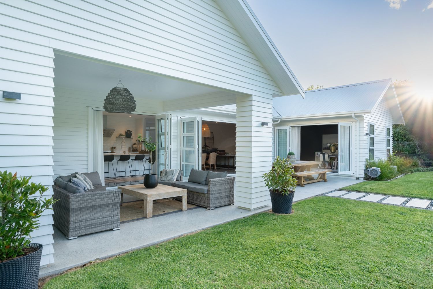 White exterior patio with outdoor lounge furniture and lawn views at sunset.