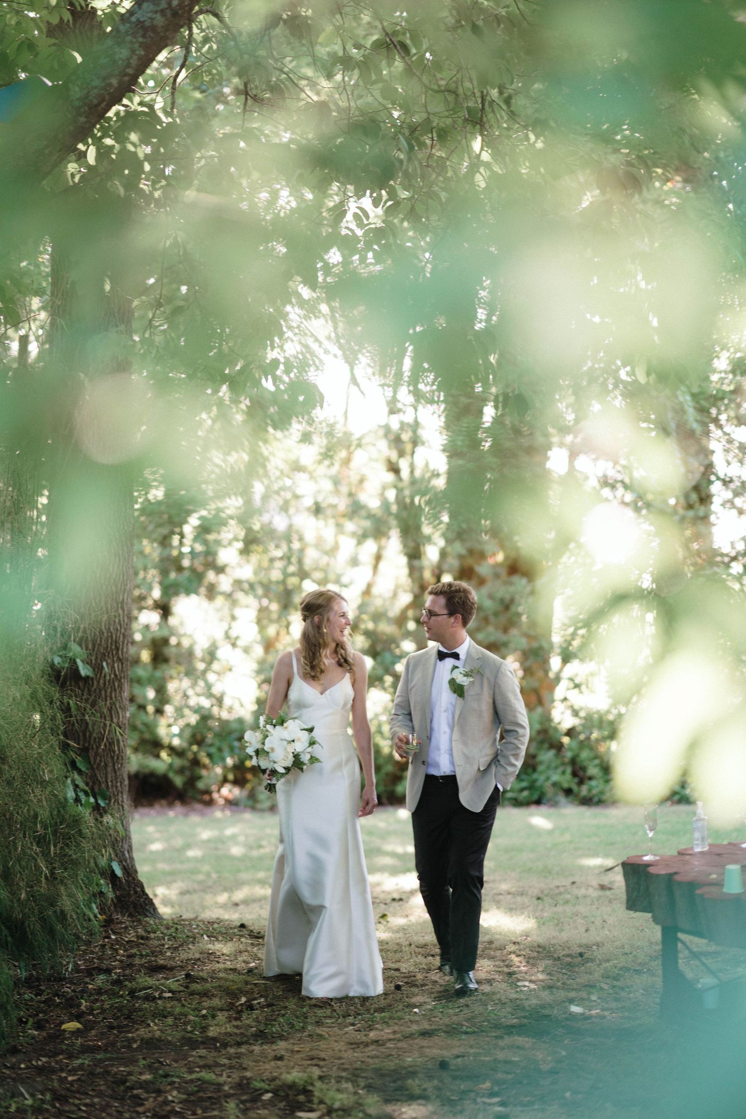 A romantic wedding couple walks along a dreamy forest path with soft bokeh lighting effects in the background.
