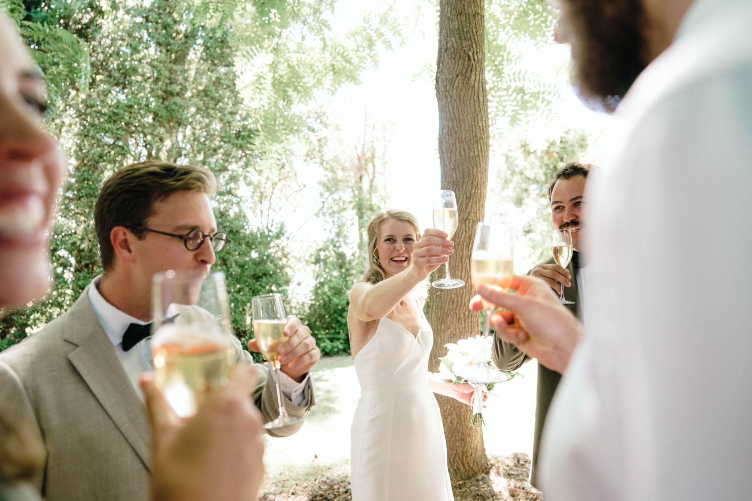 Outdoor wedding celebration under trees with guests enjoying the festivities.