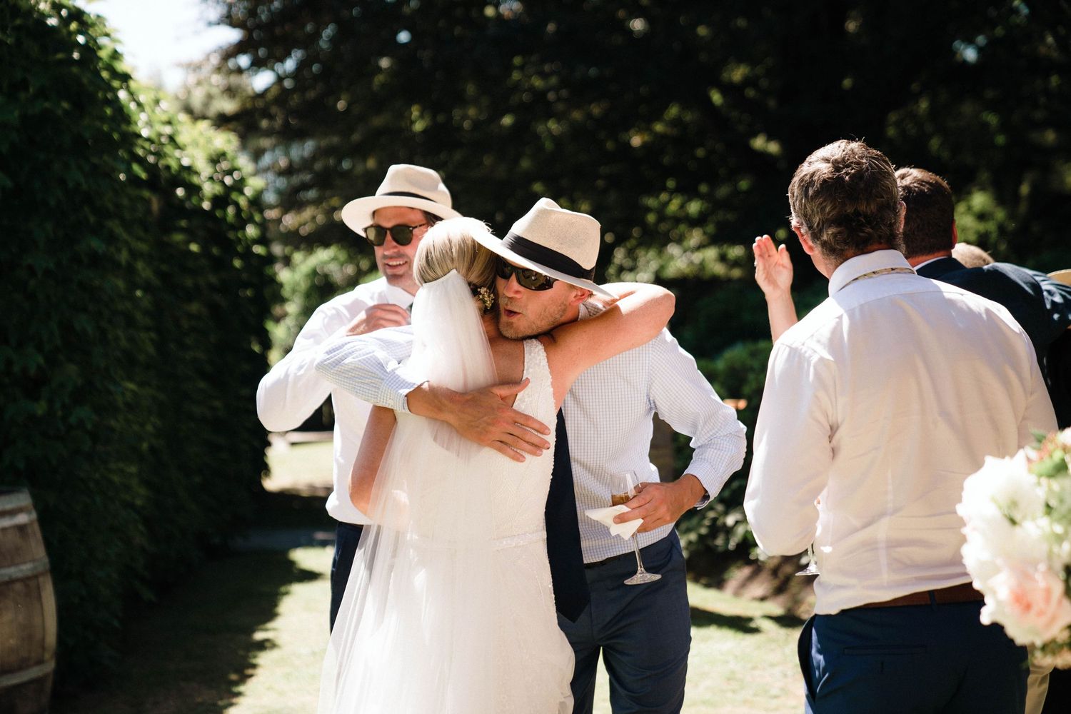 Outdoor wedding reception with guests mingling in garden setting wearing summer attire.