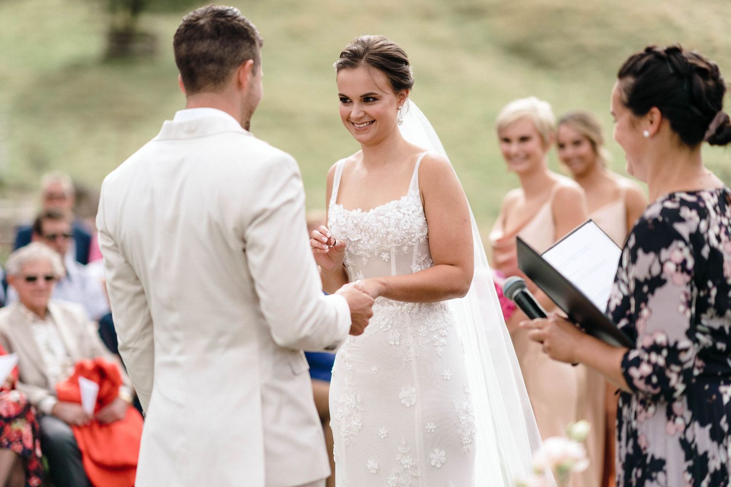 Guests watching a wedding ceremony on a grassy hillside with white chairs.