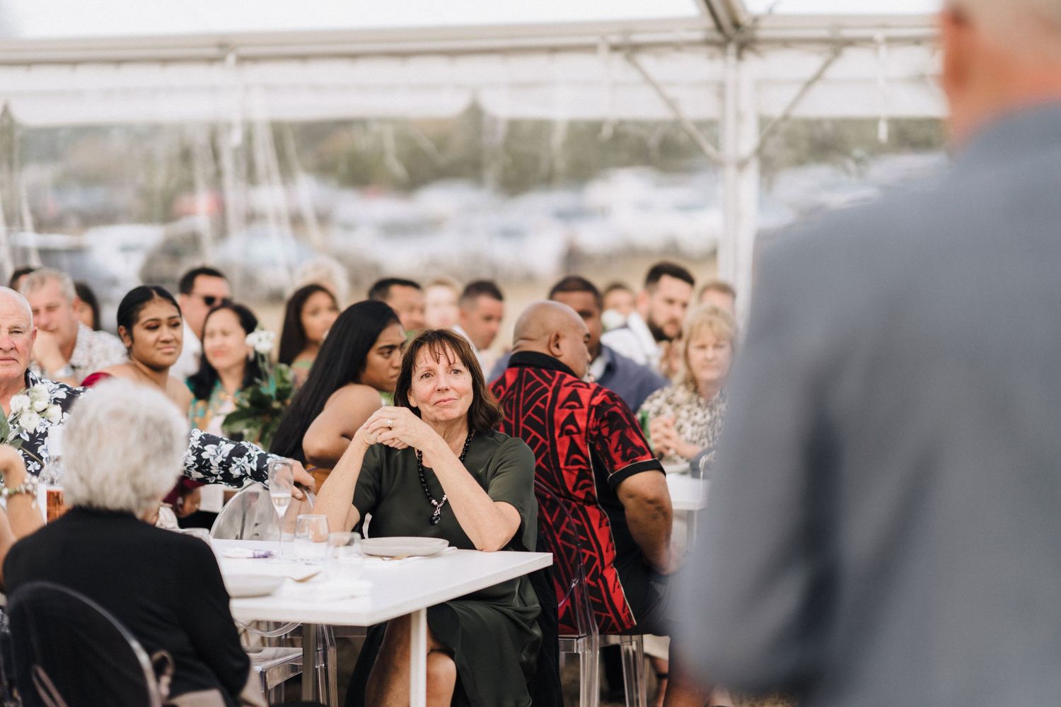 Wedding reception guests seated under white tent enjoying celebration.