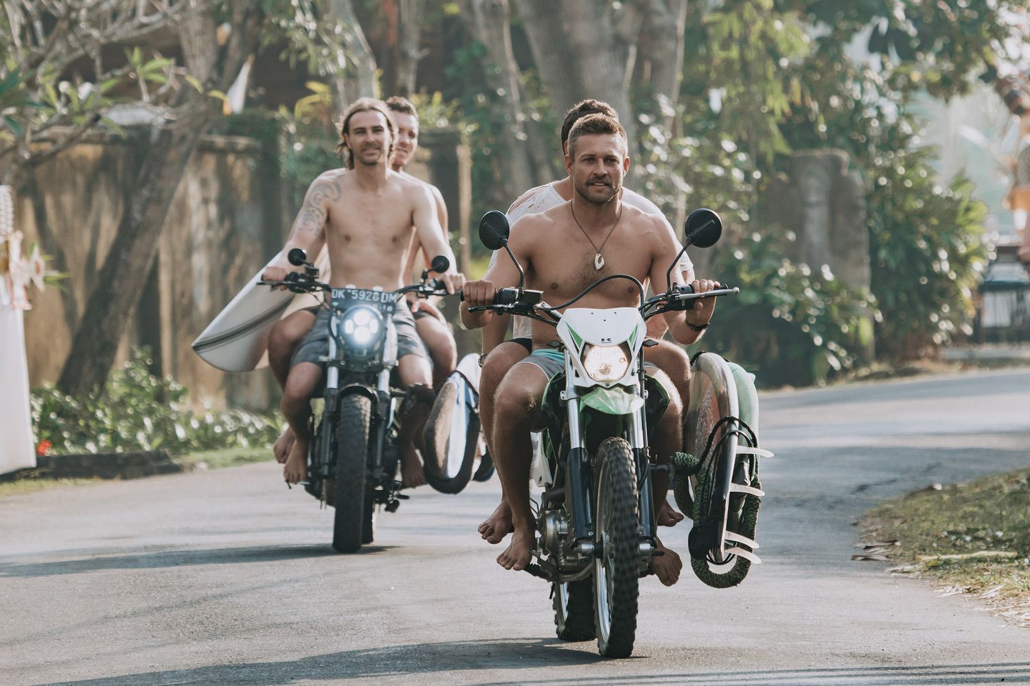 Four sequential shots of people riding vintage motorcycles through a tree-lined street on a sunny day.