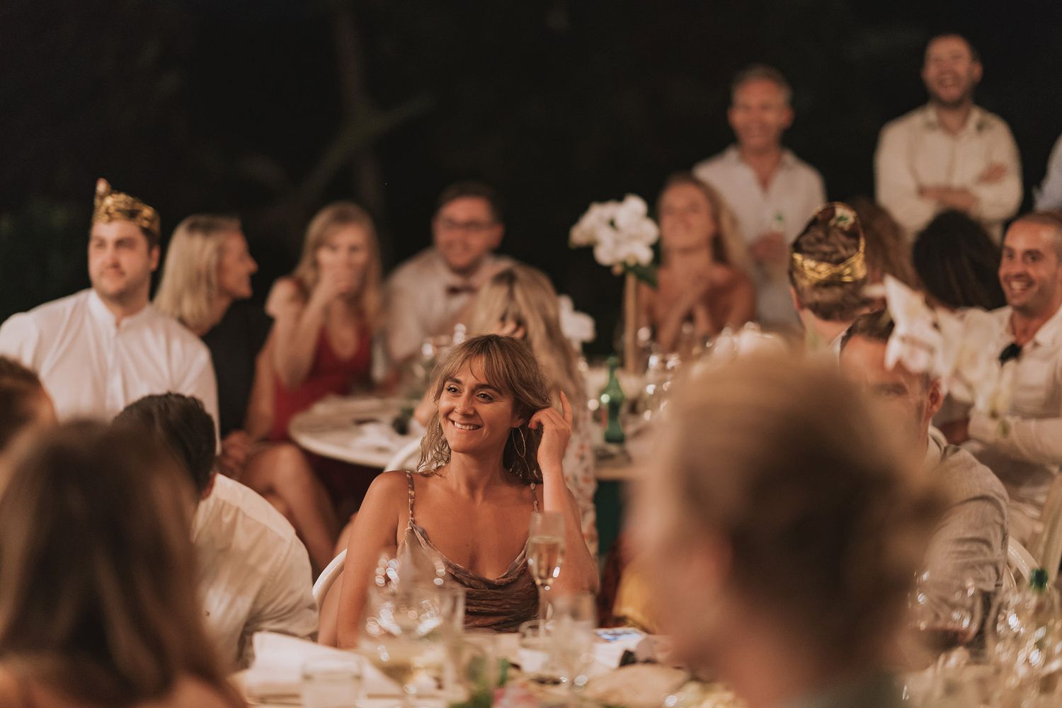 Wedding reception guests enjoying dinner under twinkling lights at an outdoor venue.