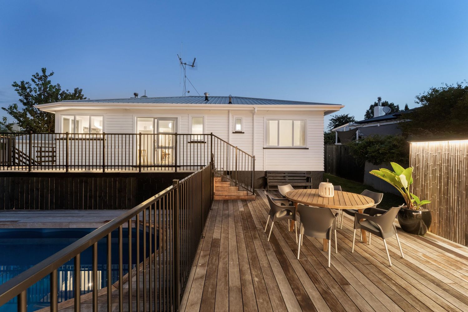 Modern white house with wooden deck and pool area lit up at dusk.