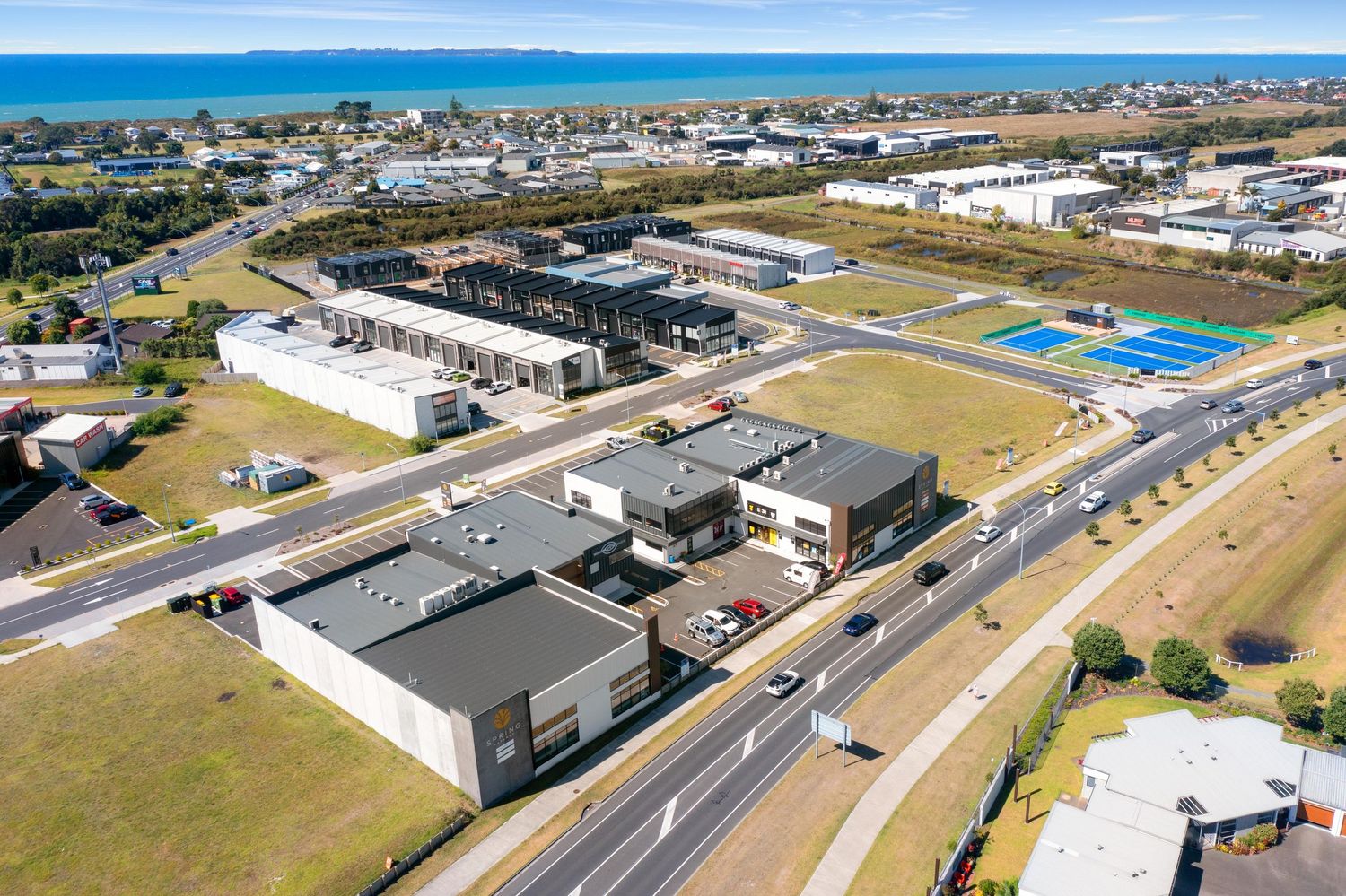 Panoramic drone shot of retail complexes and commercial developments along a busy roadway.