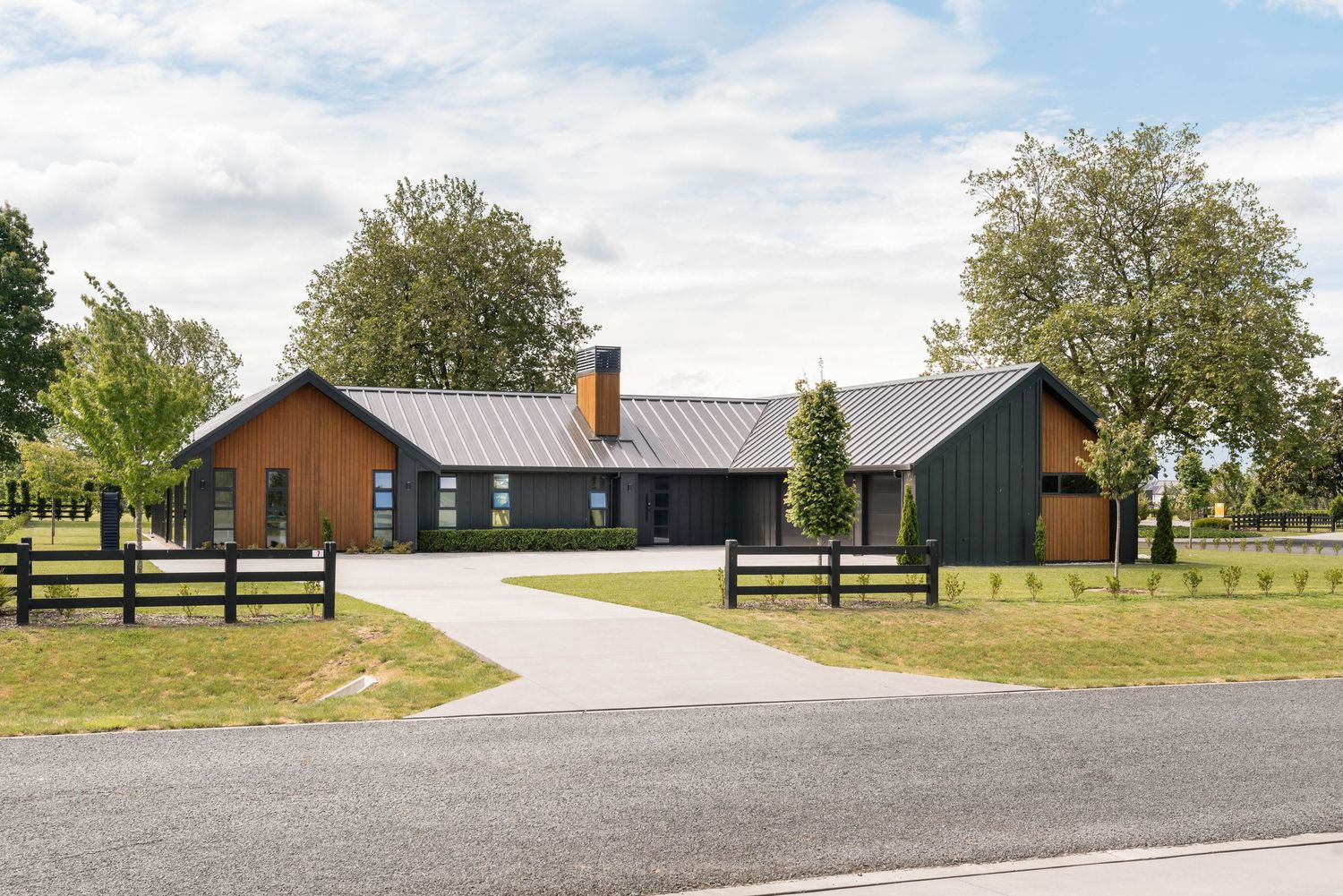 Contemporary farmhouse with dual-tone exterior featuring wood and dark panels connected by covered walkway.