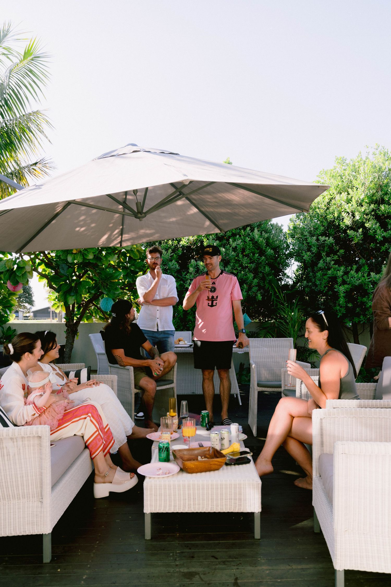 Guests enjoying a relaxing outdoor lounge area with white furniture and umbrellas at a social gathering.