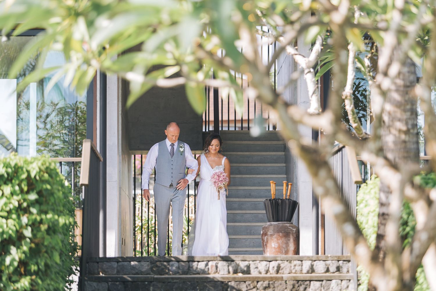 Wedding couple standing on outdoor staircase surrounded by lush greenery.
