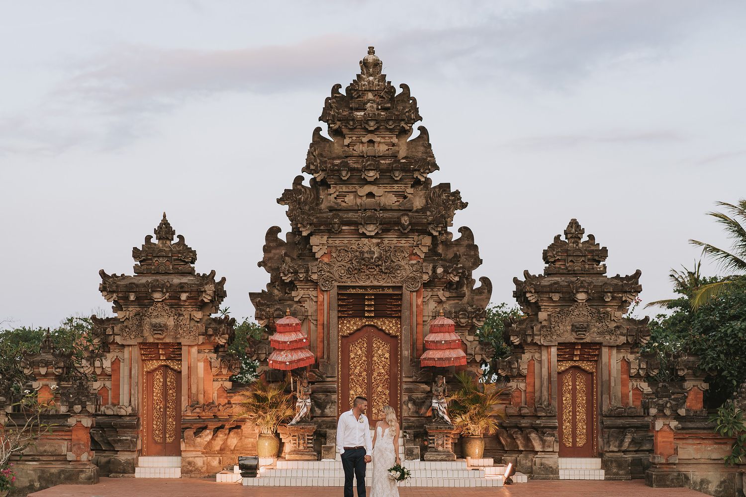 Traditional Balinese temple gates and architecture with ornate stone carvings against cloudy sky.