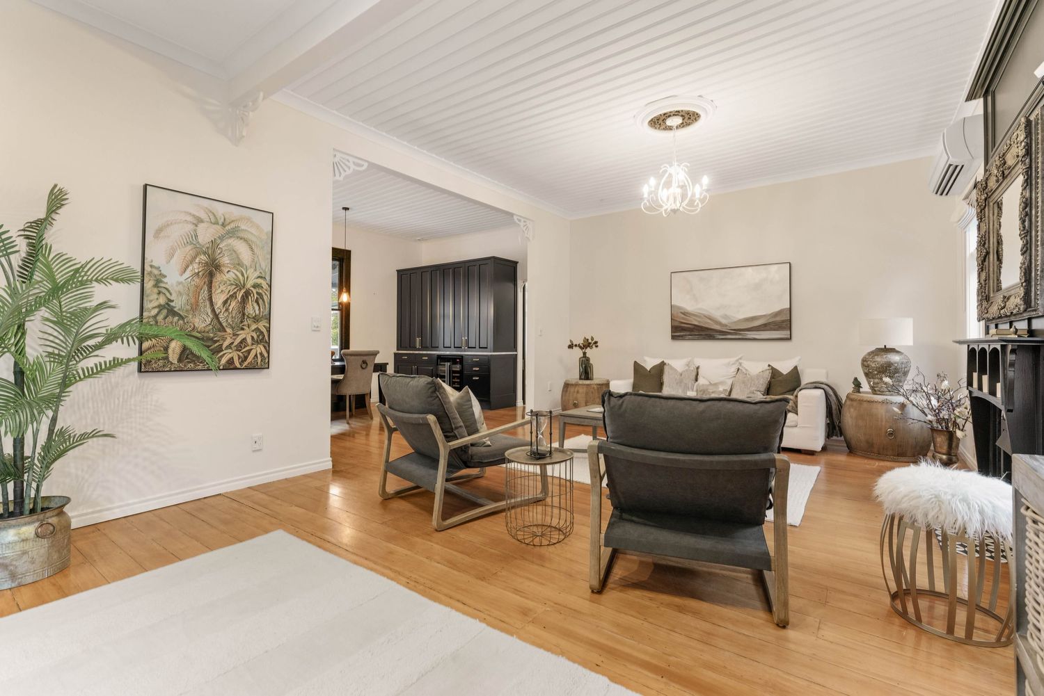 Spacious living area with white beamed ceiling, contemporary furniture, and natural light from large windows.