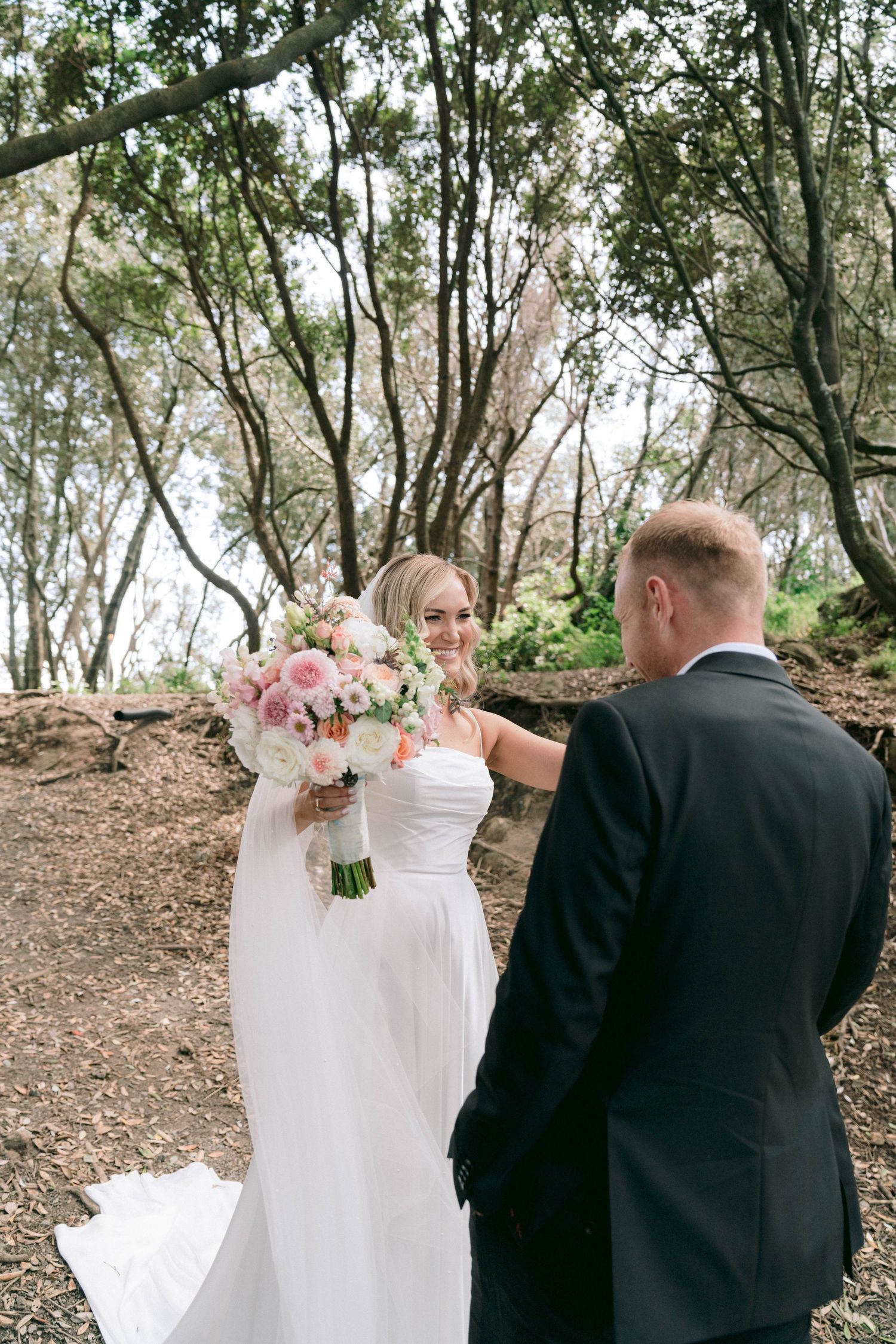 Wedding party taking photos in a wooded outdoor setting with natural lighting.