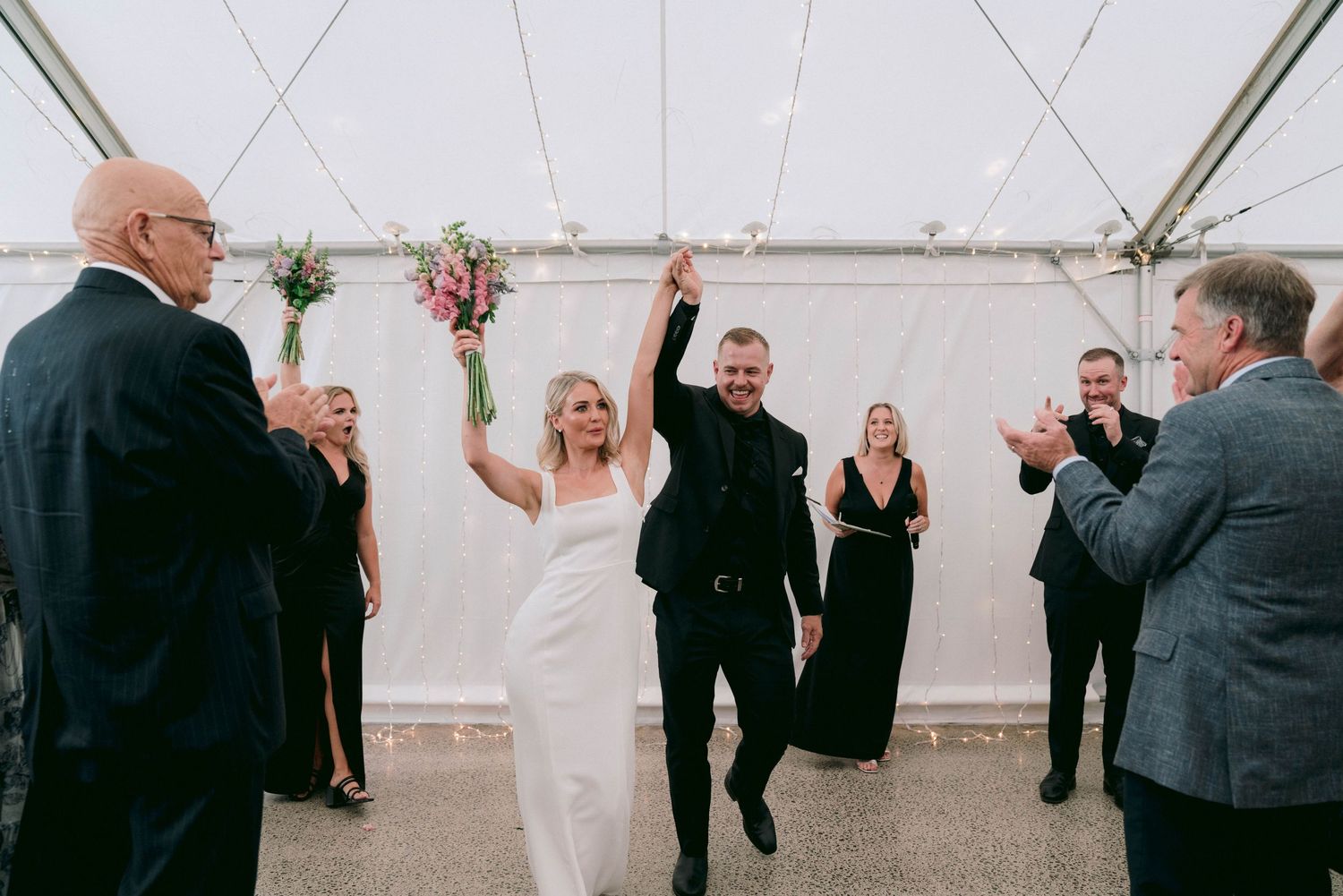 Celebratory guests dance and socialize during a wedding reception in a tented venue.