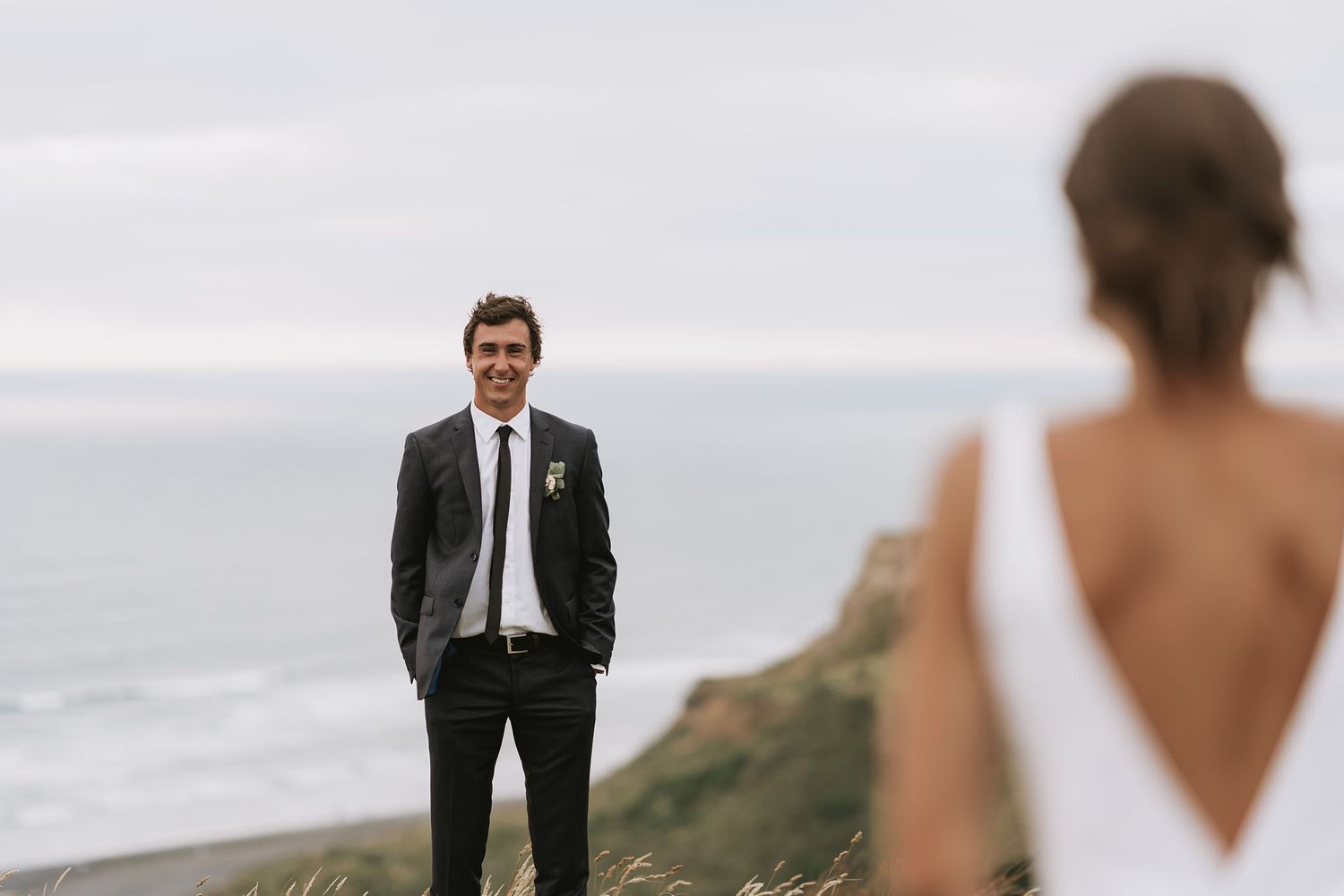 Wedding couple stands on dramatic coastal cliffs overlooking an ocean vista.