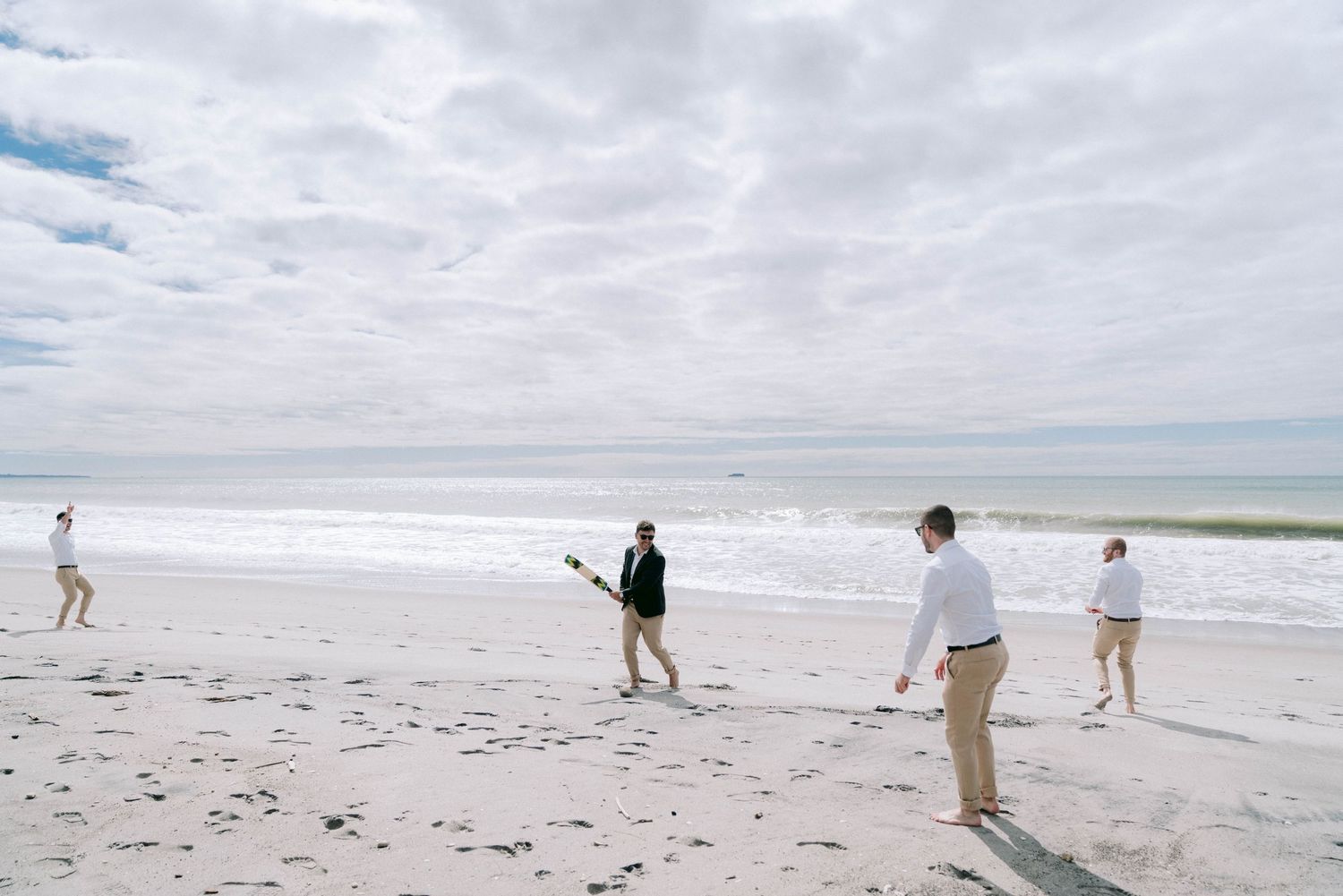 People walking and playing along a sandy beach under cloudy skies on a peaceful day at the seashore.