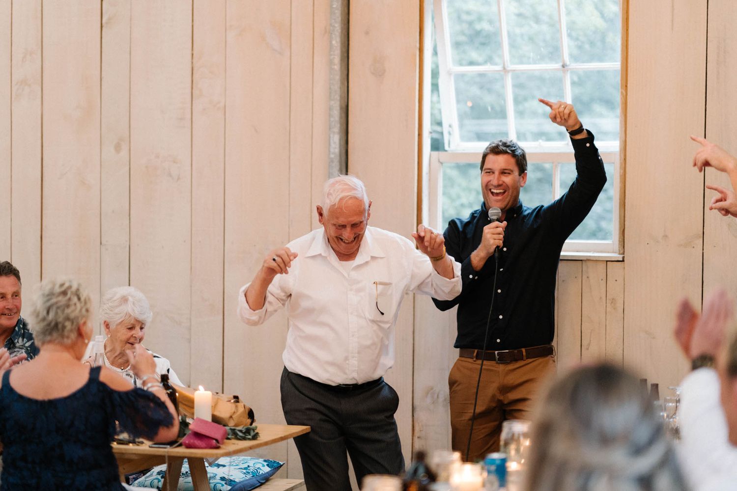 Wedding reception celebration inside a rustic barn venue with wooden paneled walls and natural lighting.