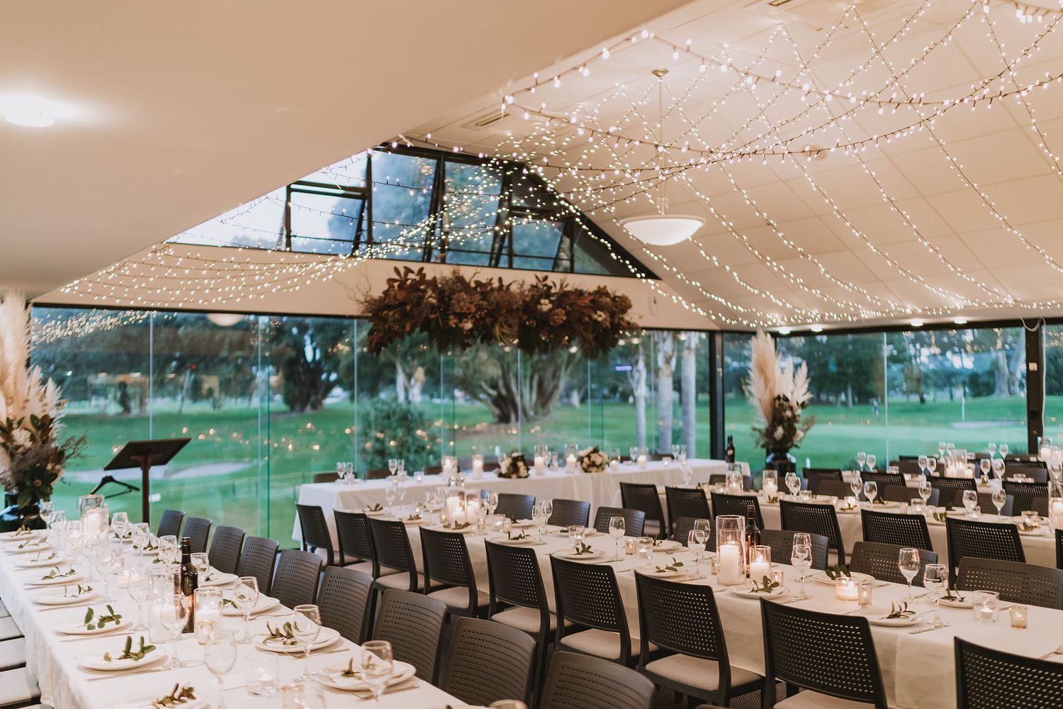 An elegant wedding reception setup in a clear tent pavilion with long tables and string lights creating a romantic atmosphere.