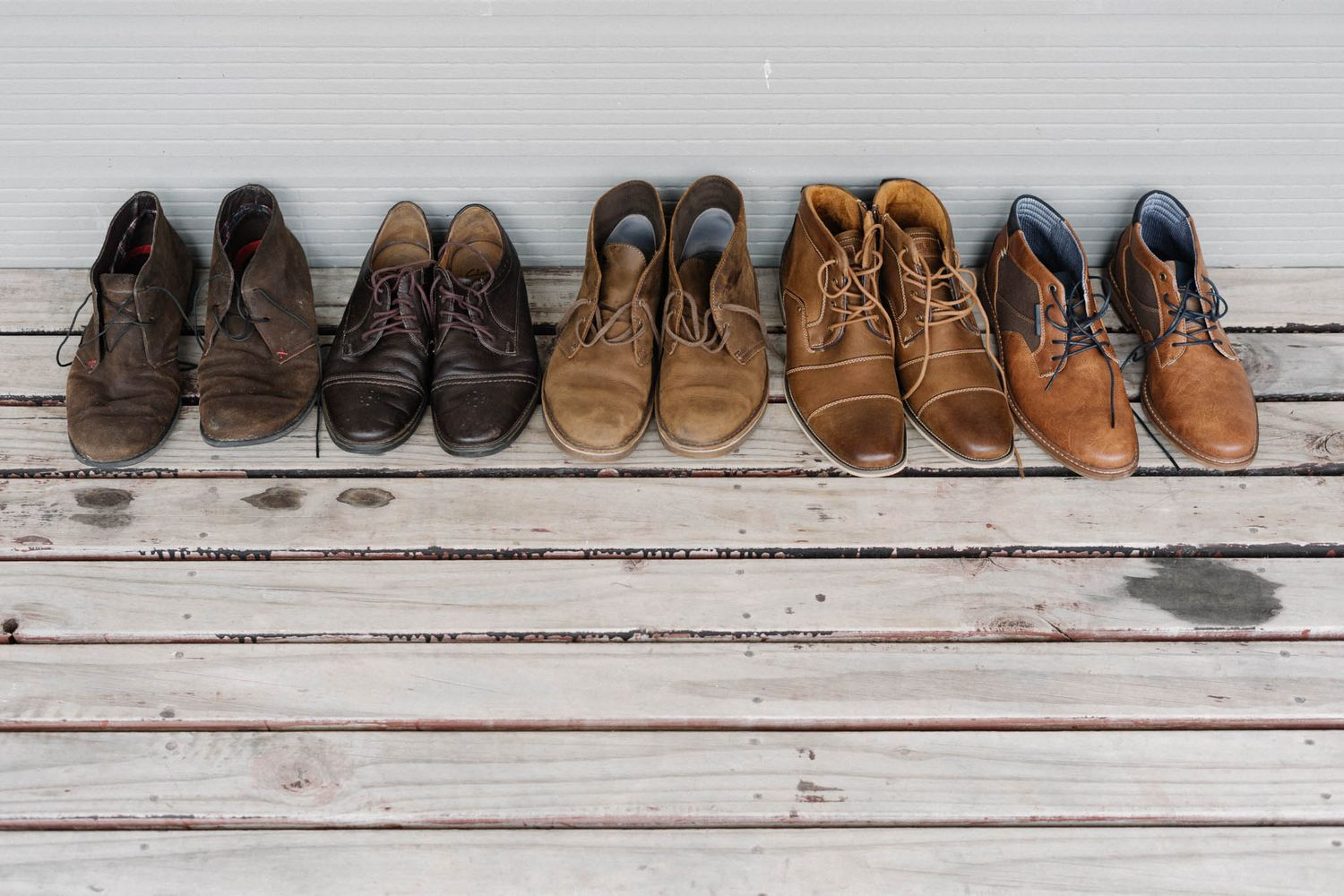 Seven pairs of casual shoes and boots arranged in a line on a rustic wooden plank floor.