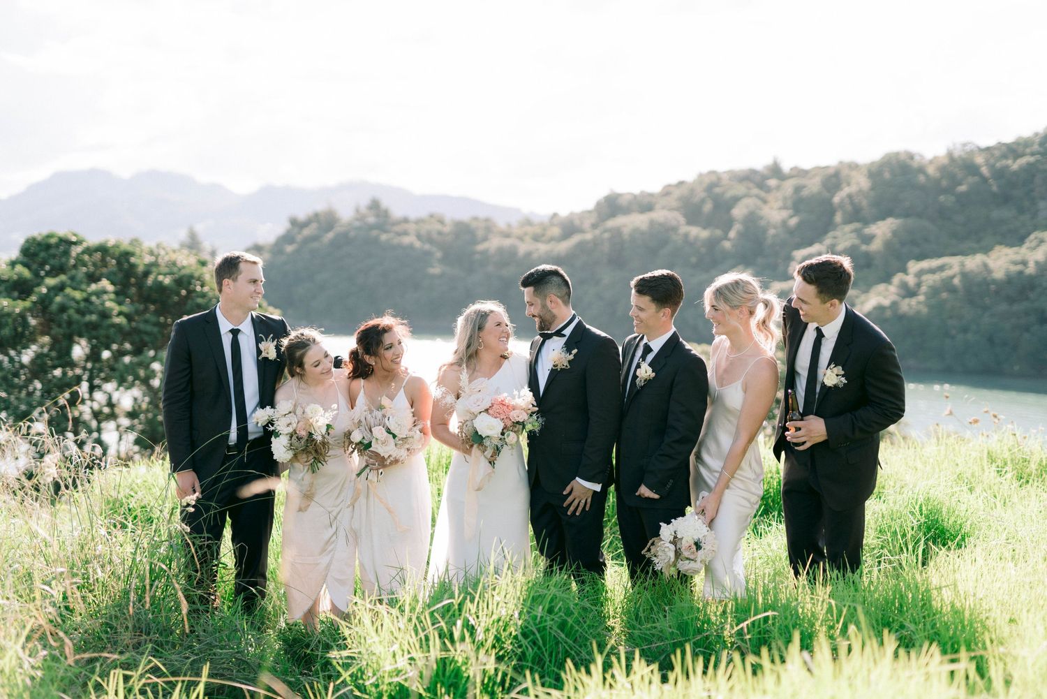 Wedding party poses together in a lush green field during a sunny outdoor celebration.