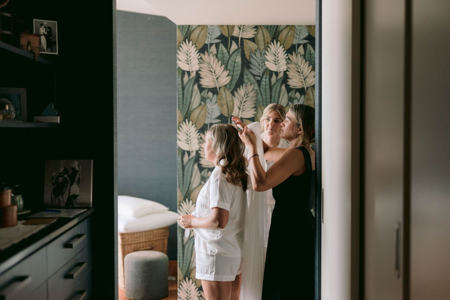 Two people standing together by a wall with tropical leaf wallpaper in a bedroom interior.