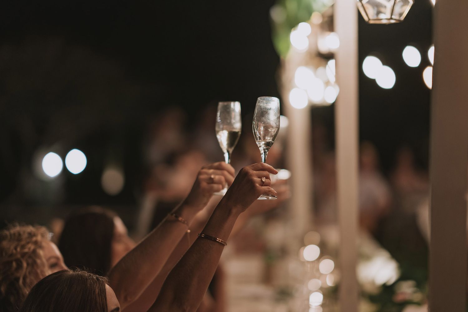 Champagne glasses being raised in celebration during dimly lit reception.
