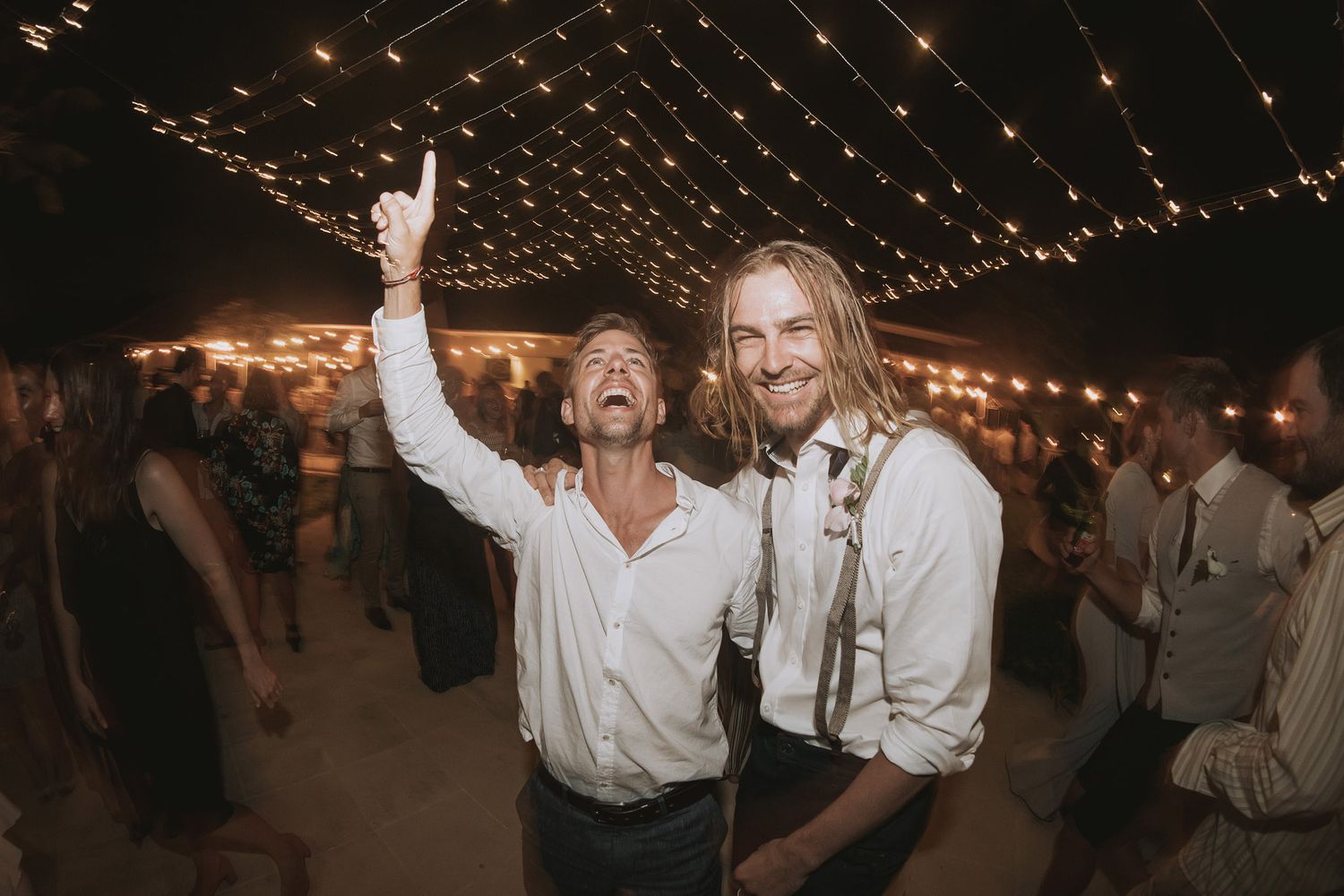 Wedding celebration under twinkling string lights with guests dancing and enjoying festivities.
