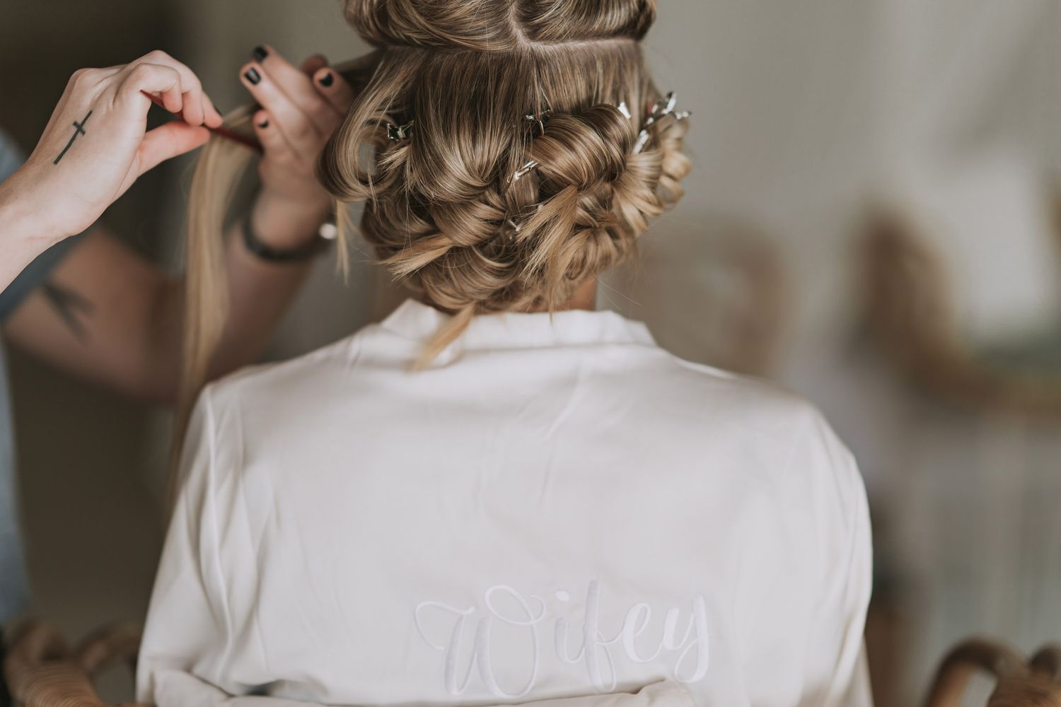 Hair stylist working on an intricate braided updo hairstyle with a person wearing a white top.