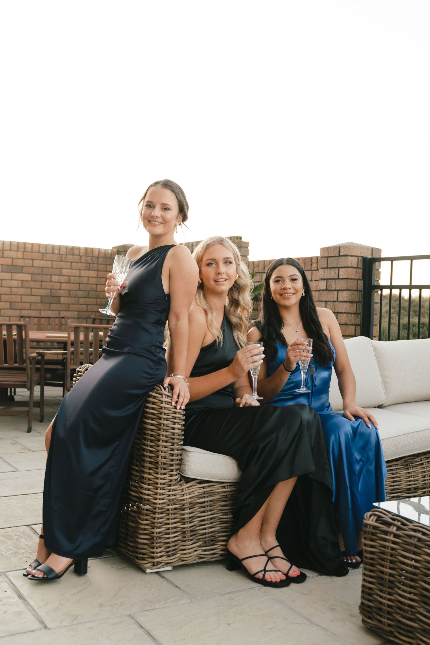 Three women relaxing on wicker patio furniture during sunset gathering.