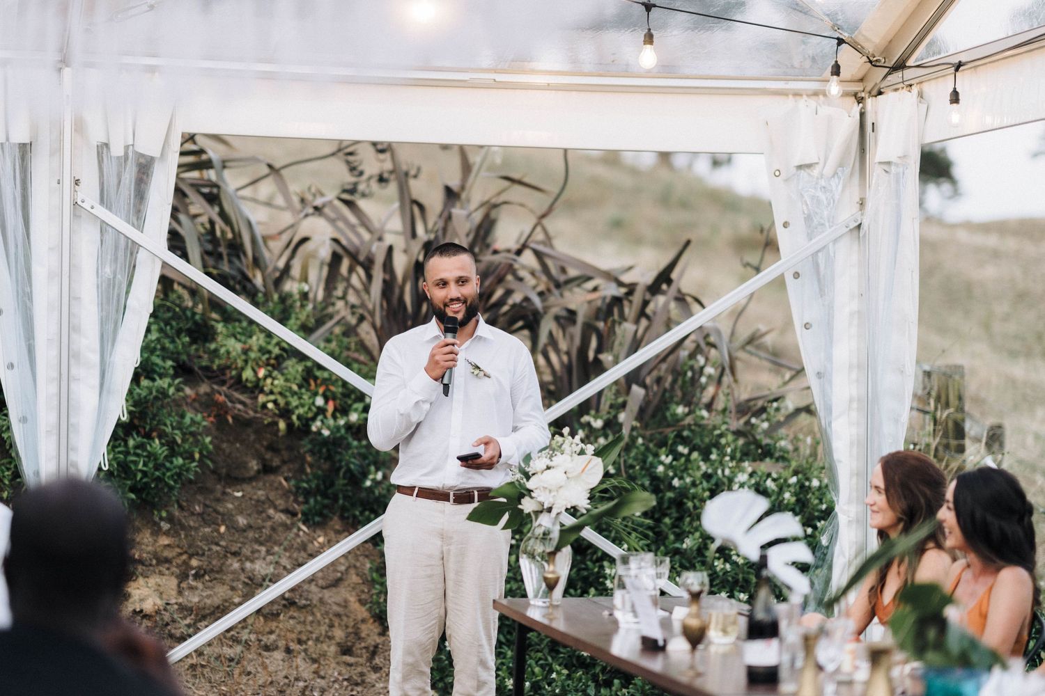 Outdoor wedding reception setup with white tent and floral decorations.
