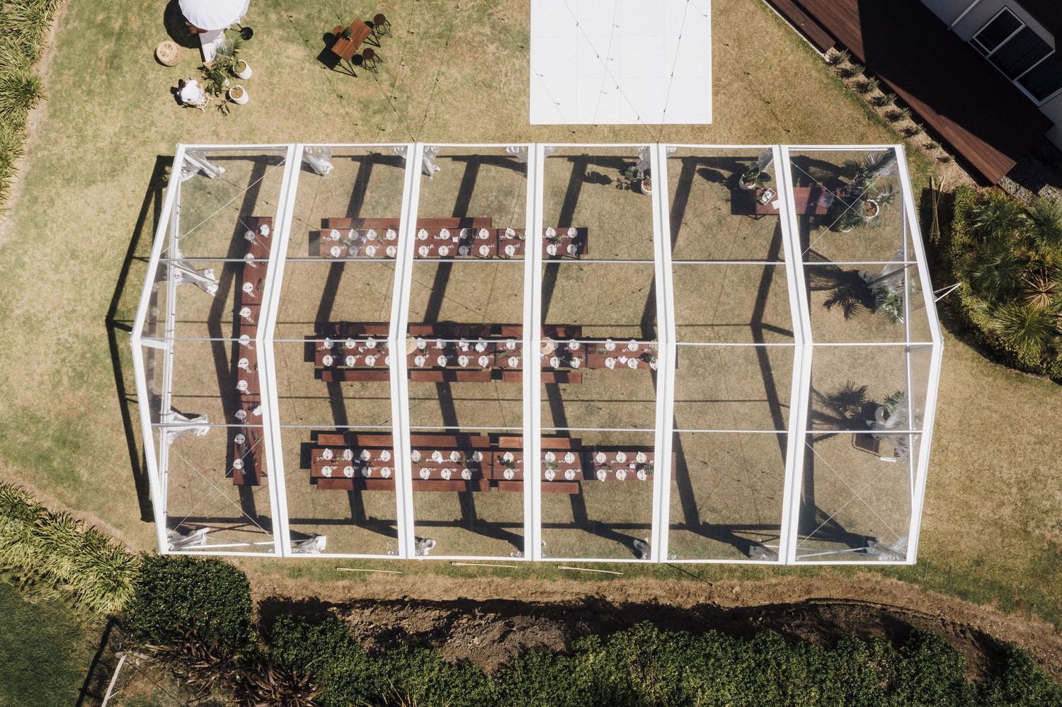 Aerial view of an outdoor wedding ceremony setup with rows of chairs arranged under a white tent structure.