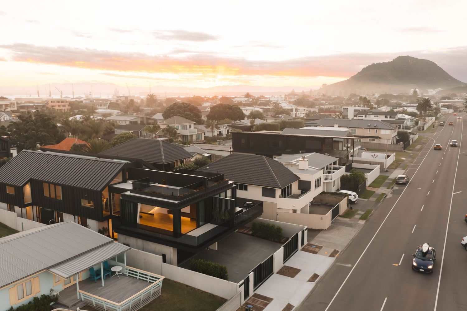 Modern residential homes line a suburban street at sunset with warm golden lighting.