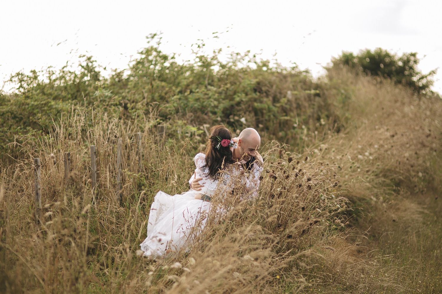 Couple embraces in tall grass field during golden sunset engagement photo session.