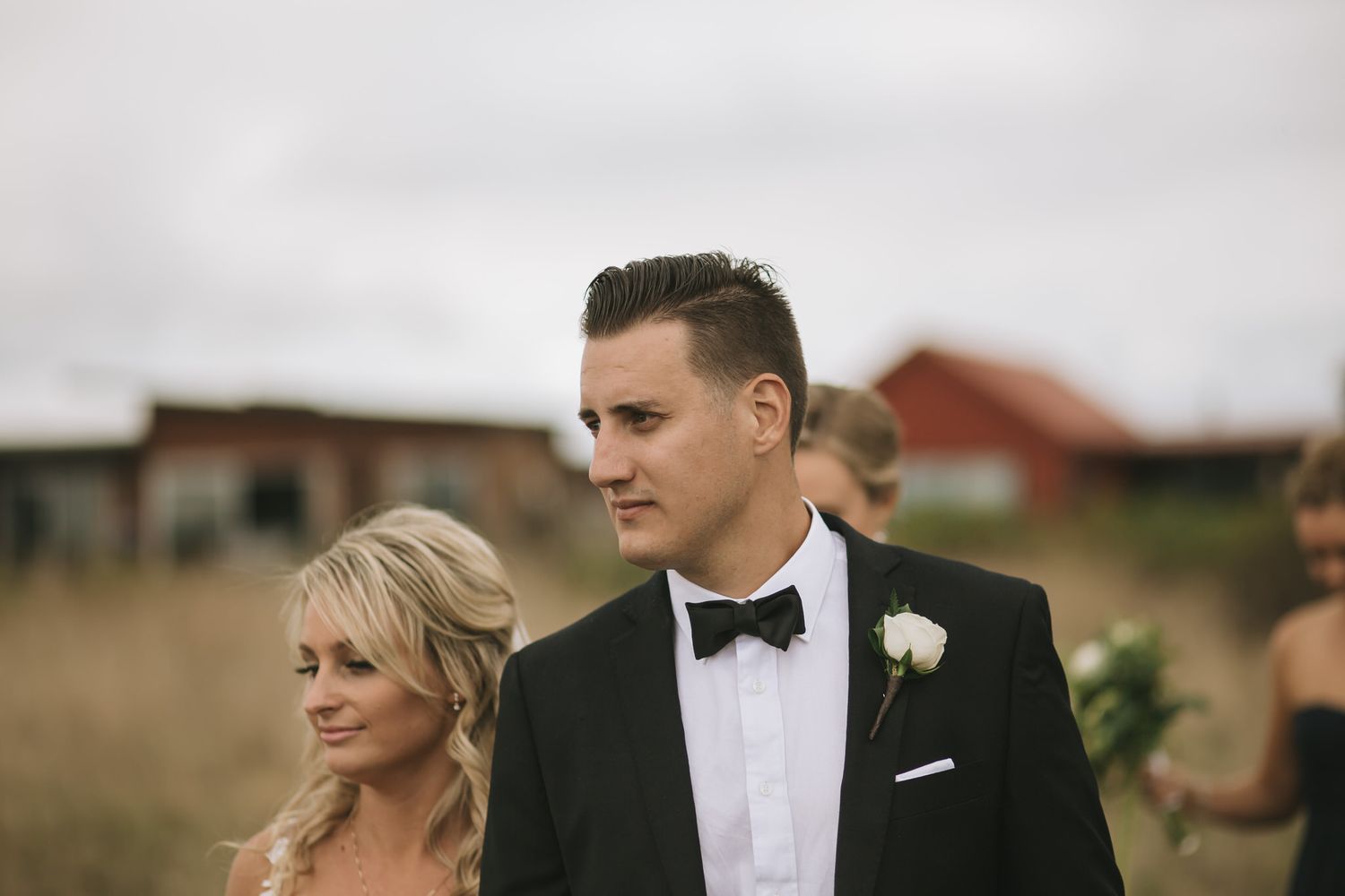 Wedding couple in elegant attire walk together outdoors with scenic backdrop on overcast day.