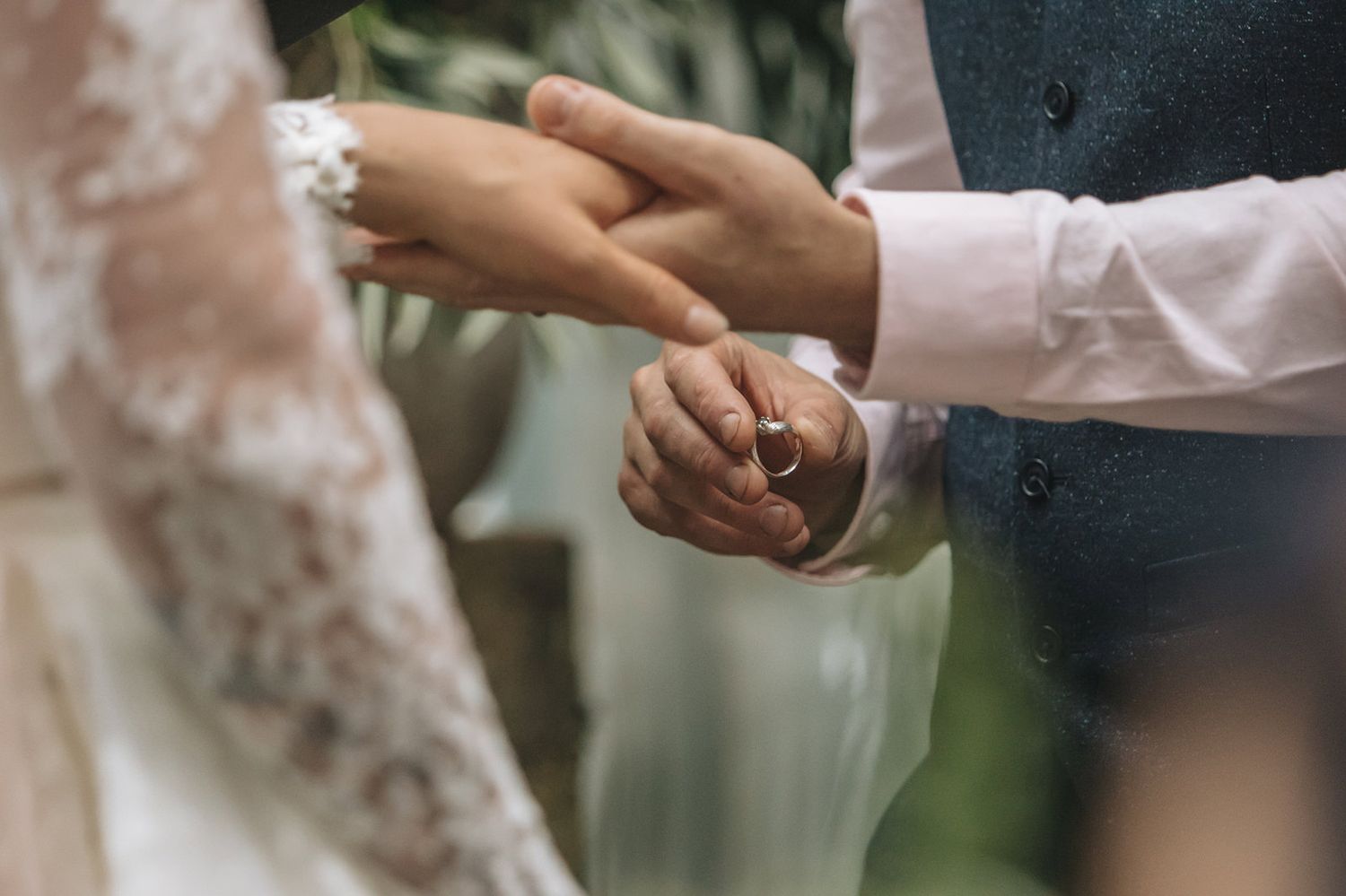 A row of hands with wedding rings touch fingers in a romantic gesture against a blurred green background.