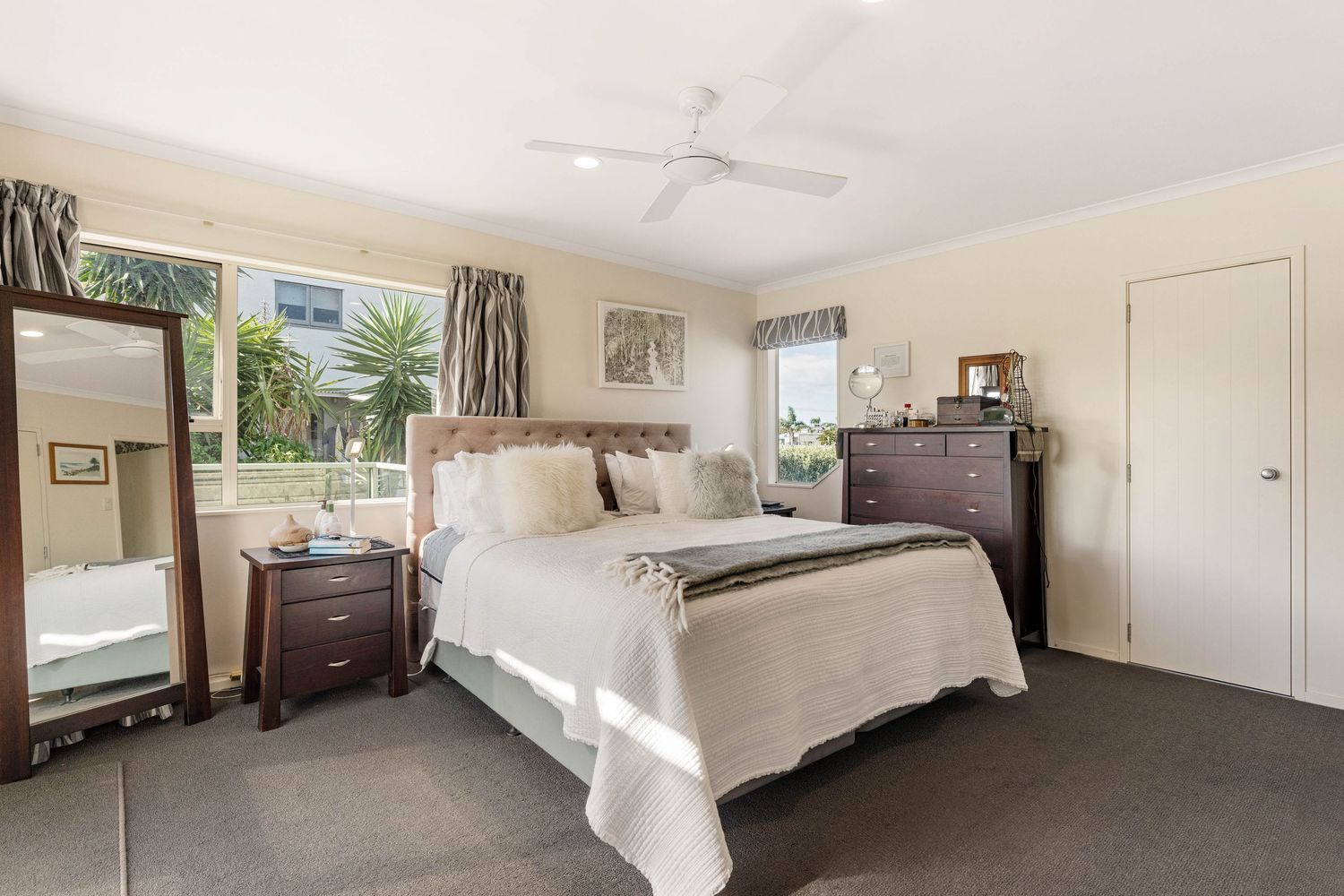 Spacious master bedroom with white bedding, wood furniture, and garden views through window.