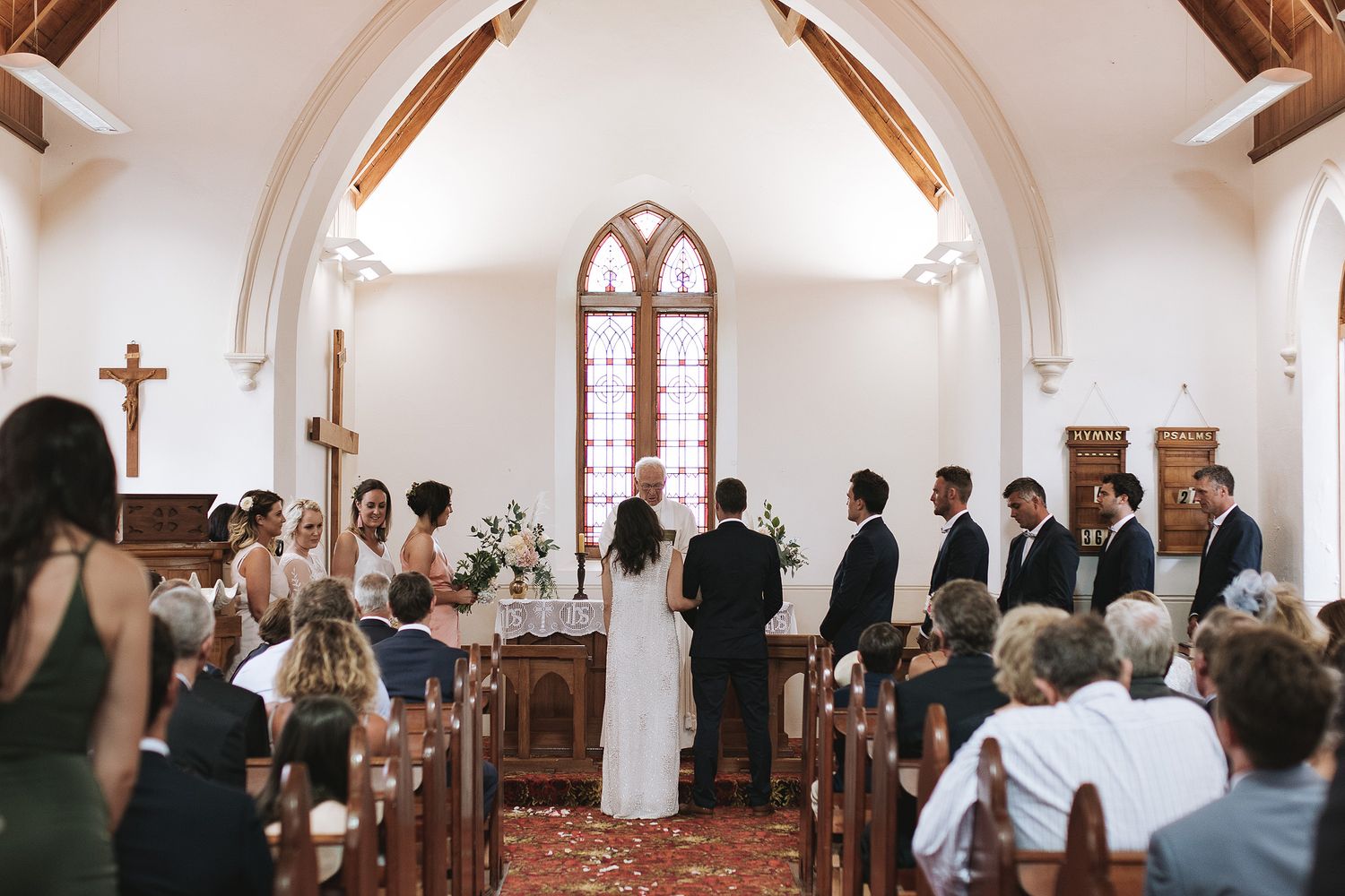 Wedding ceremony inside a traditional church with arched ceiling, wooden beams and stained glass windows.