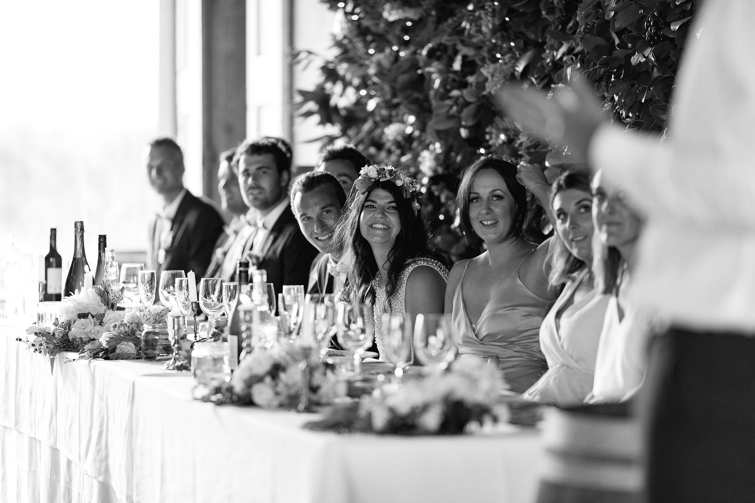 Wedding reception guests sit at long decorated tables during an outdoor celebration at sunset.