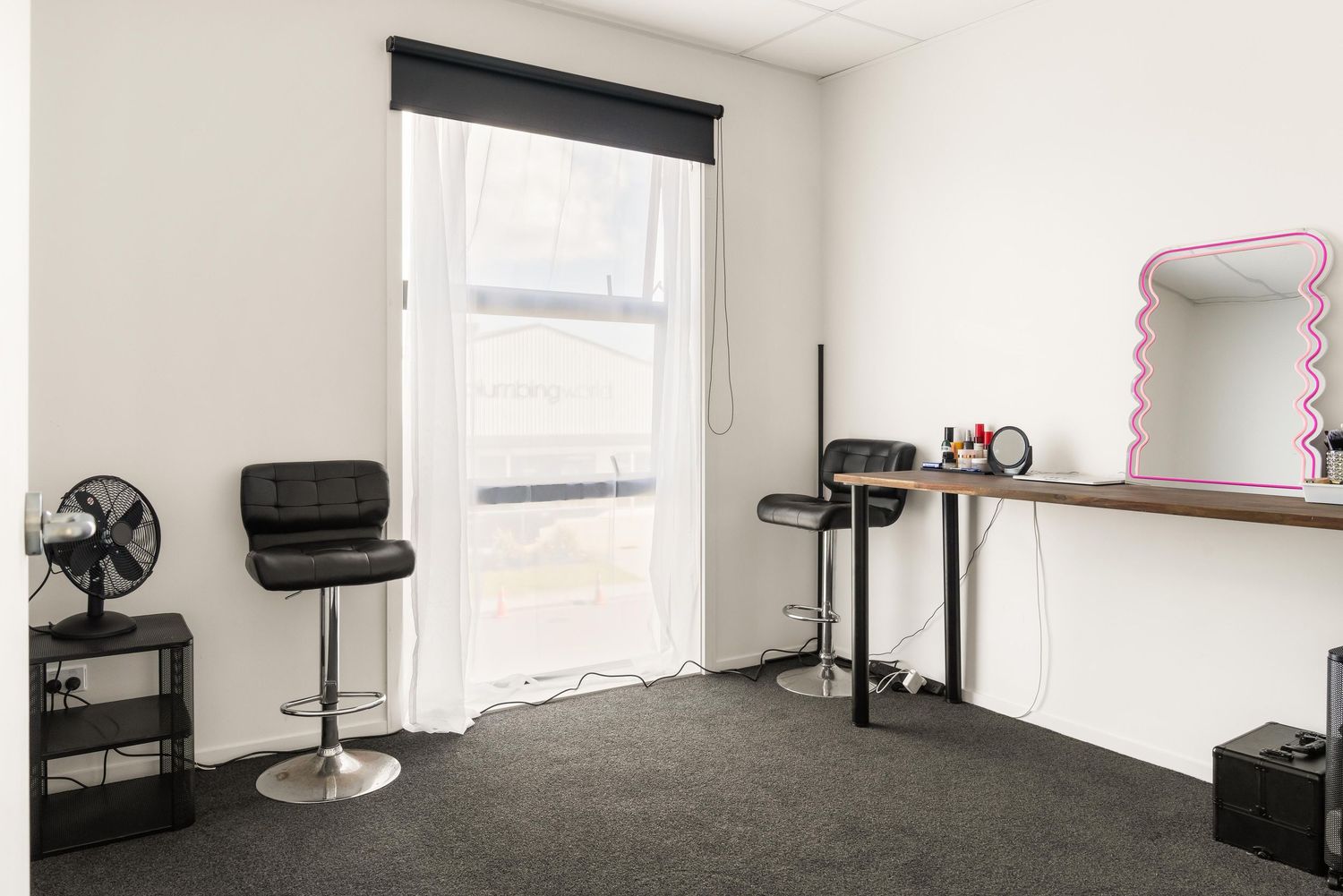 Simple dressing room with black bar stool, mirror, and window with natural light.