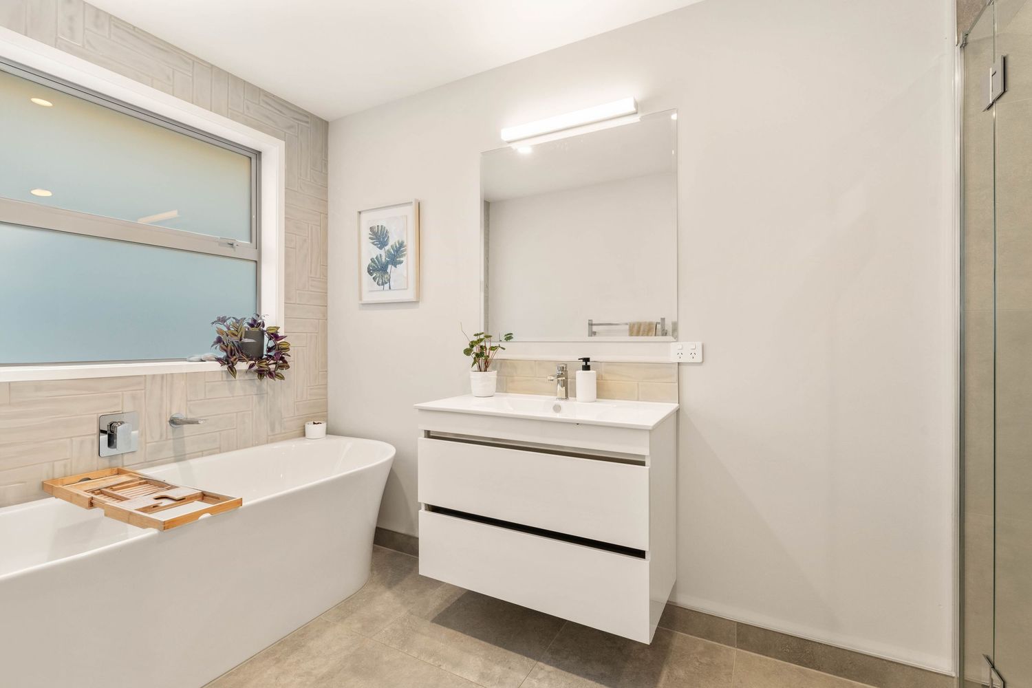 Modern white bathroom with floating vanity, large mirror, and freestanding tub.