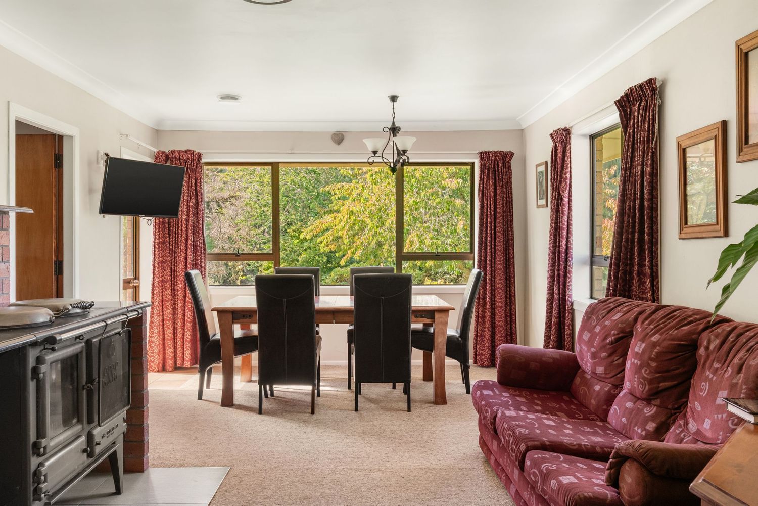 Cozy living room with burgundy couch, dining area and large windows overlooking nature.