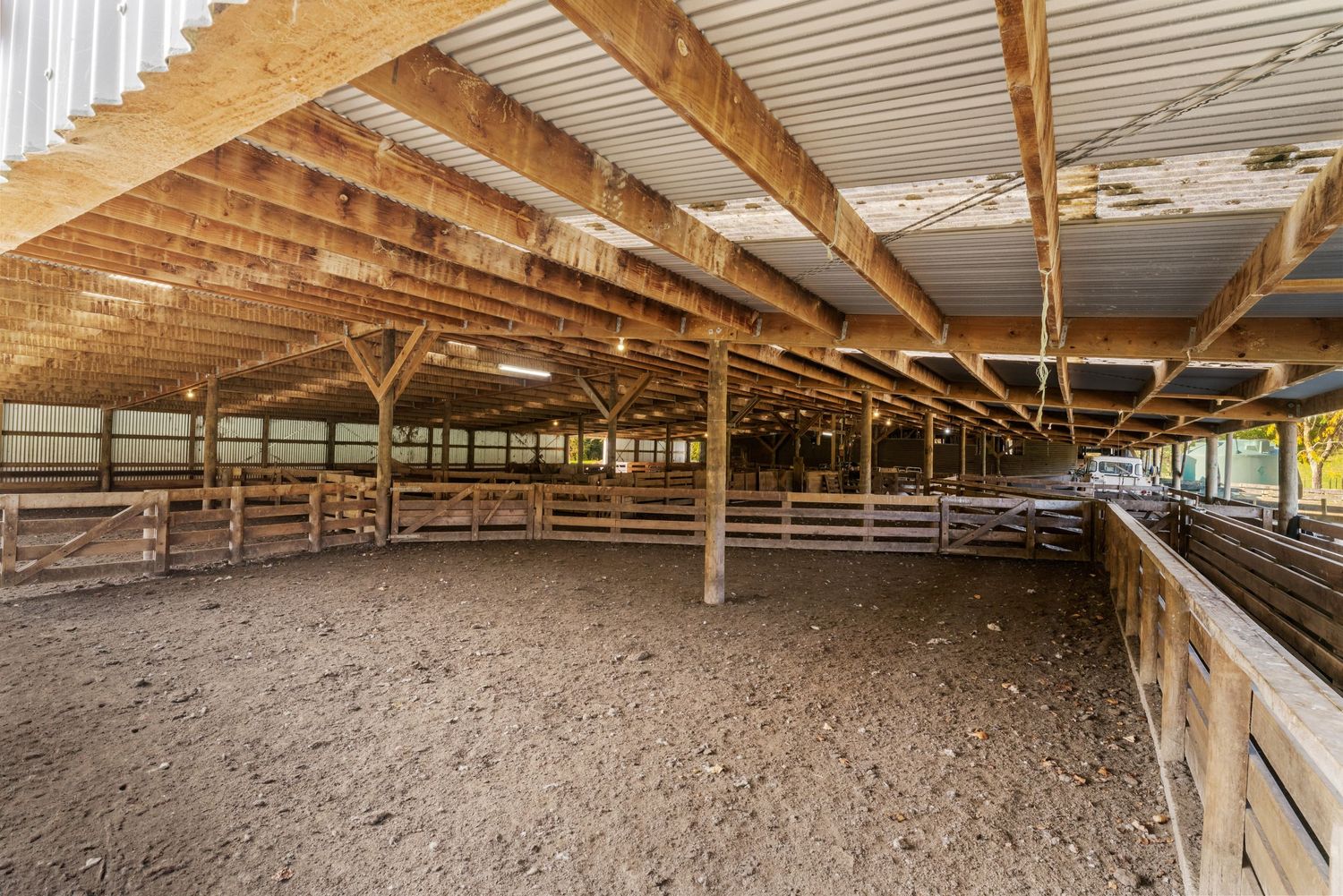 Long horse stable interior with wooden beams, metal roof, and dirt floor.