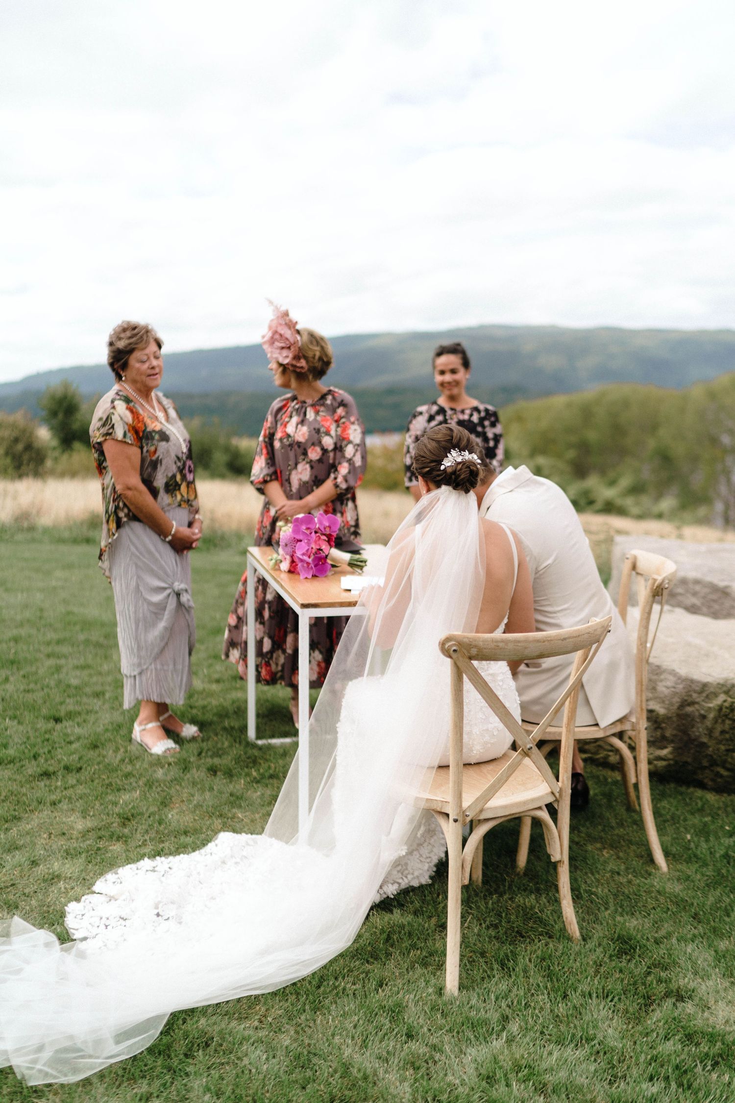 Wedding ceremony seating arrangement with white chairs and flowing fabric on green grass.
