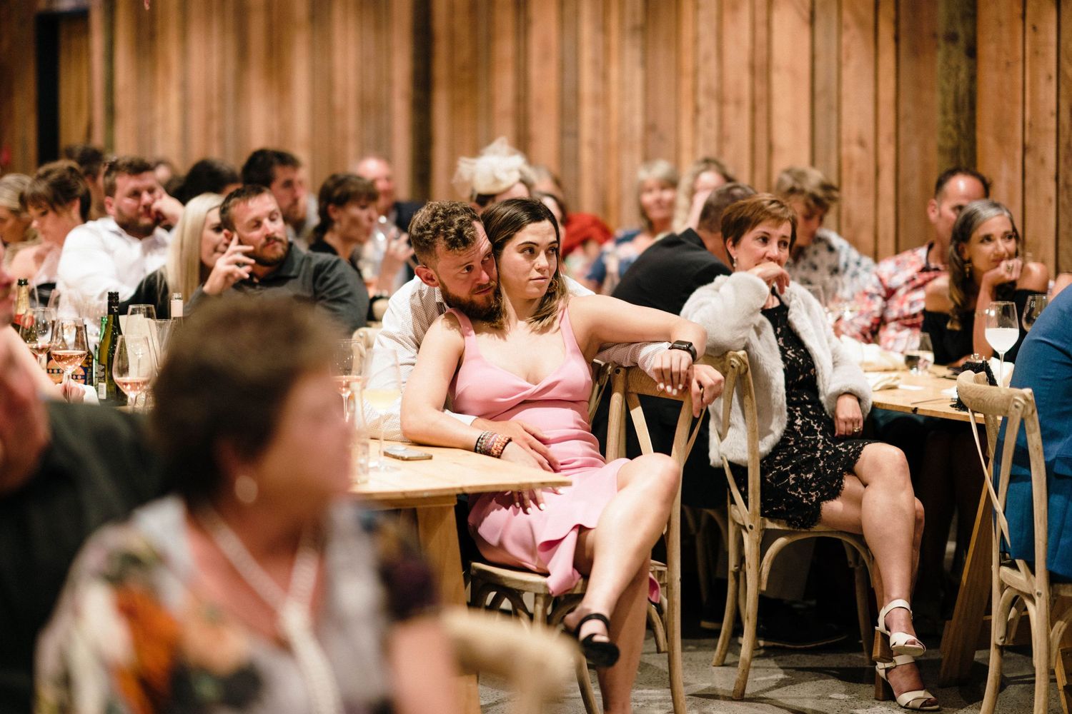 Wedding guests seated at long tables in rustic wooden reception venue.