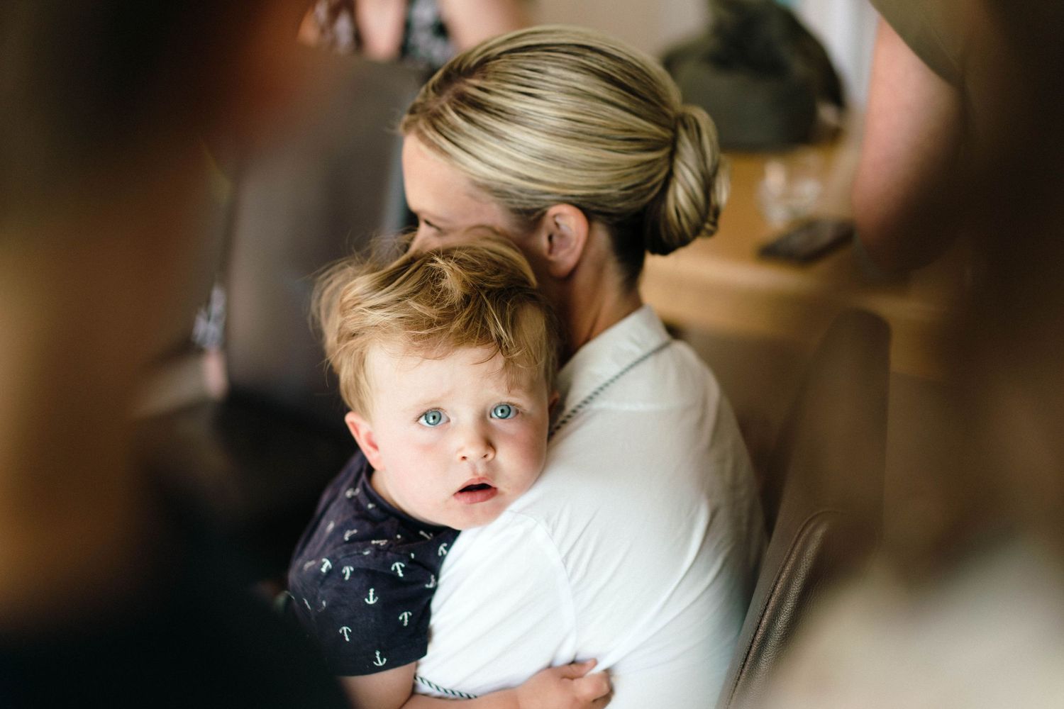 A tender moment captured between a parent and young child with blonde hair in a soft-focus indoor setting.