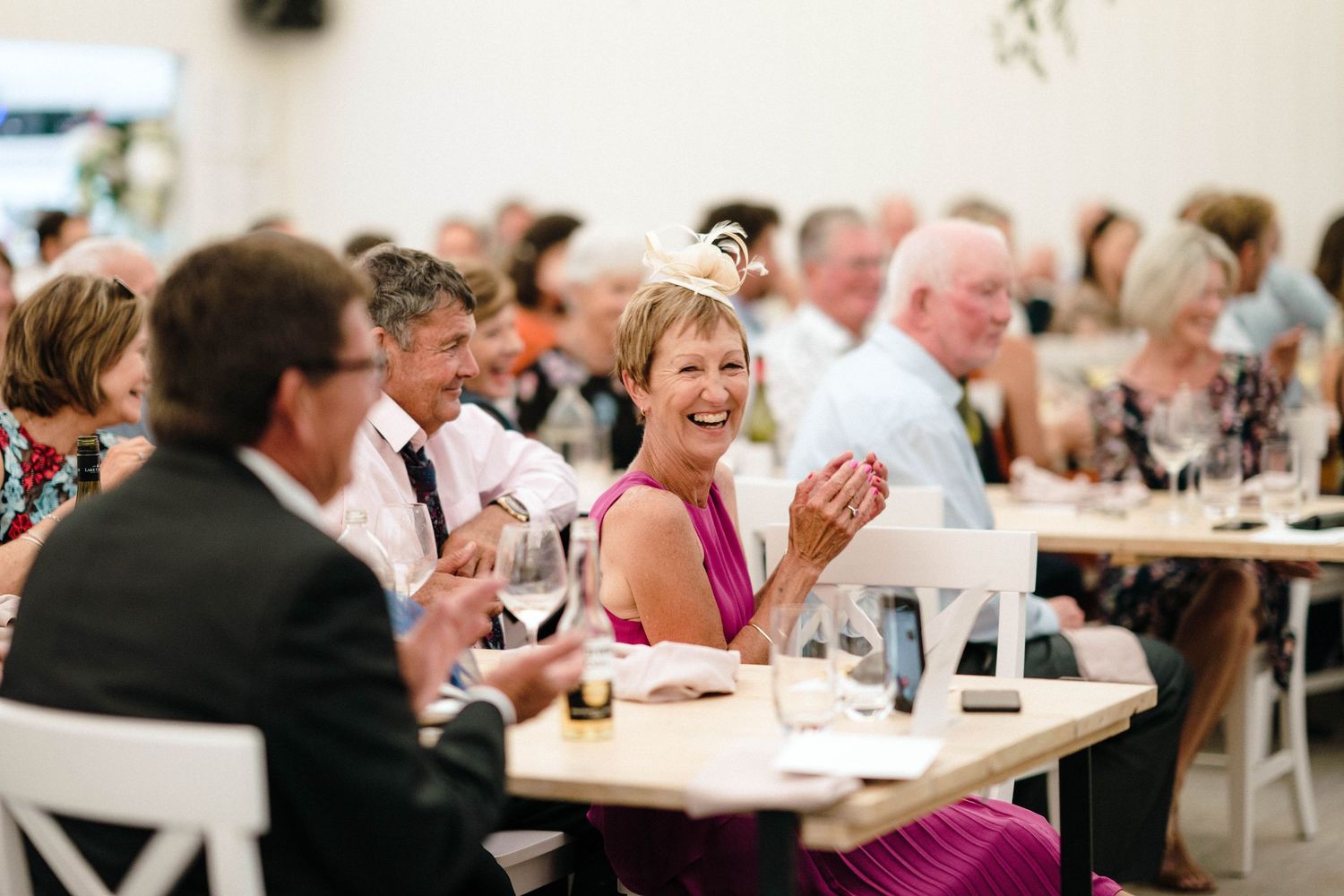 Wedding reception guests laughing and enjoying dinner at outdoor tables.