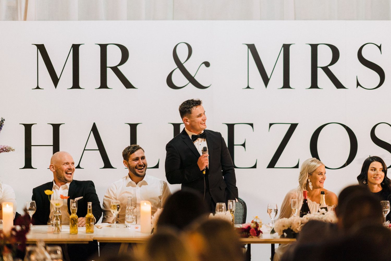 A reception celebration with guests seated at tables beneath a large Mr & Mrs banner sign.